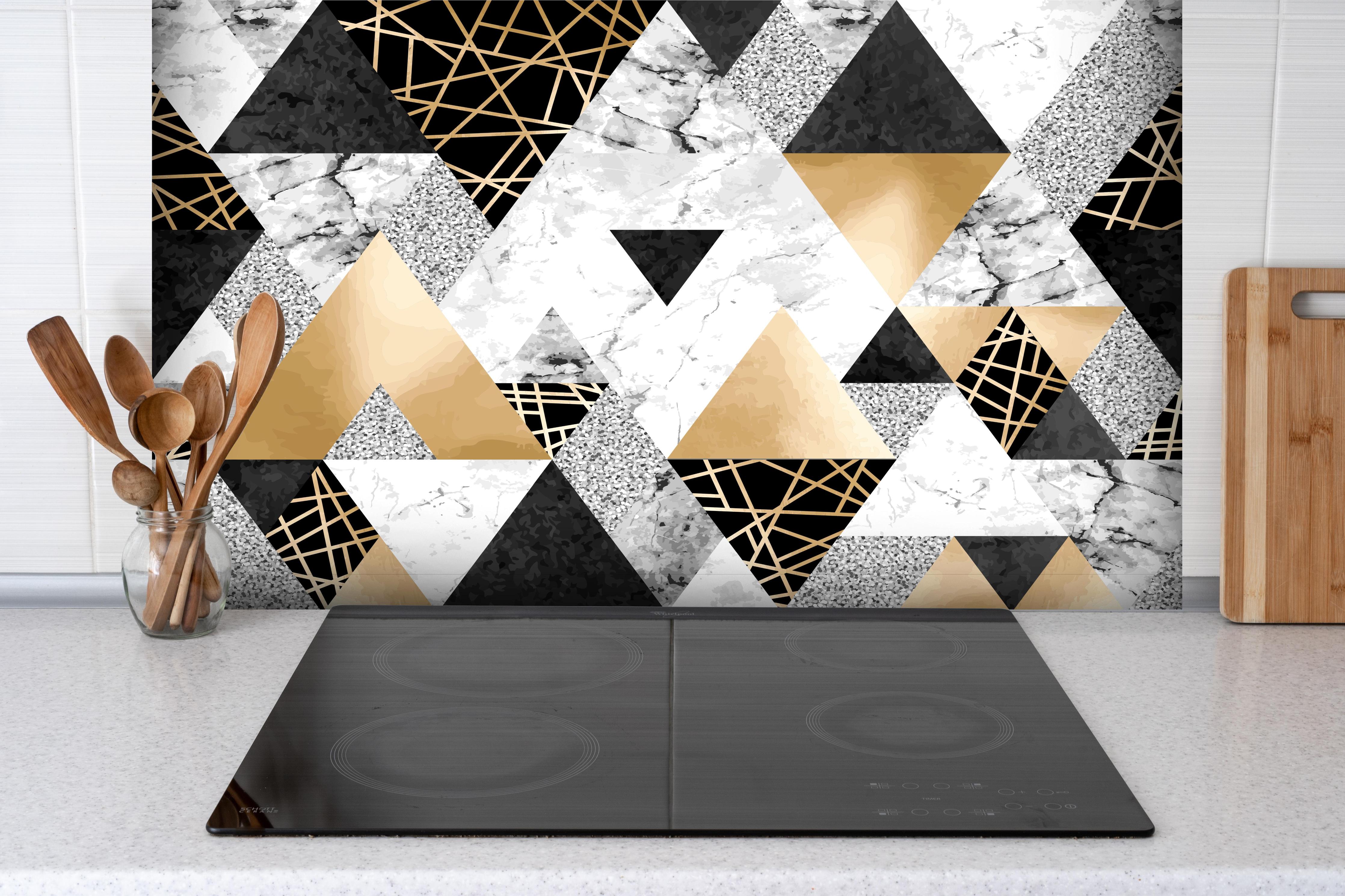 Spritzschutz - Geometrisches Muster in Gold, Schwarz und Weiß hinter einem Cerankochfeld zwischen Holz-Kochutensilien
