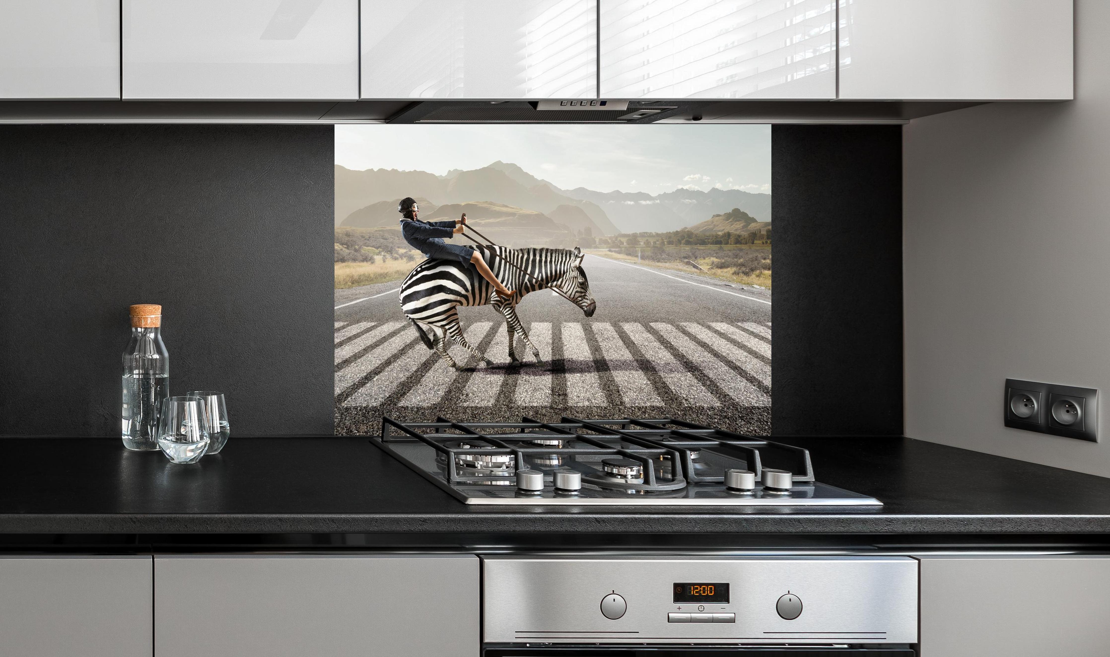 Spritzschutz - Geschäftsfrau reitet Zebra in Landschaft hinter einem Cerankochfeld zwischen Holz-Kochutensilien

