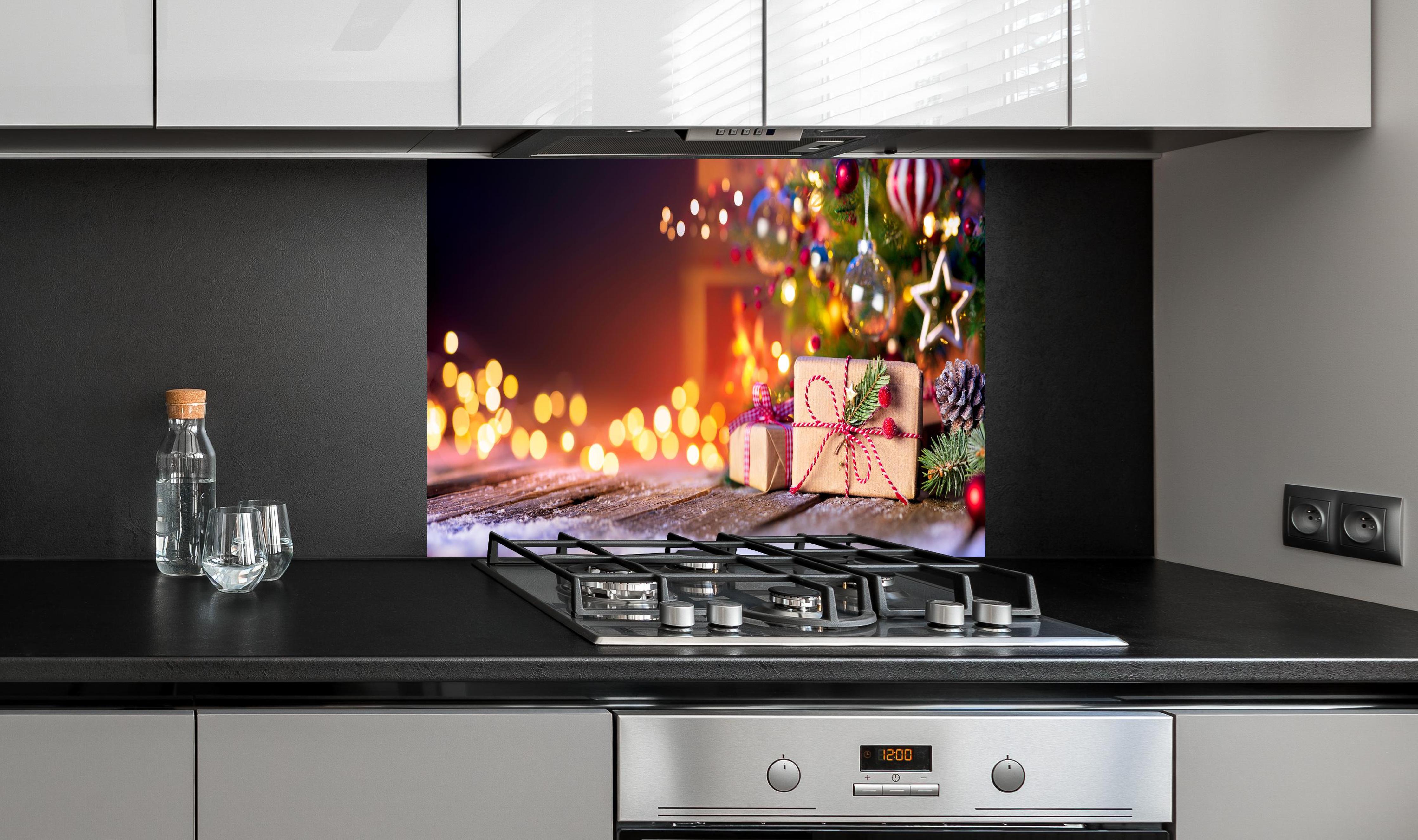 Spritzschutz - Geschenke unter dem Weihnachtsbaum hinter einem Cerankochfeld zwischen Holz-Kochutensilien
