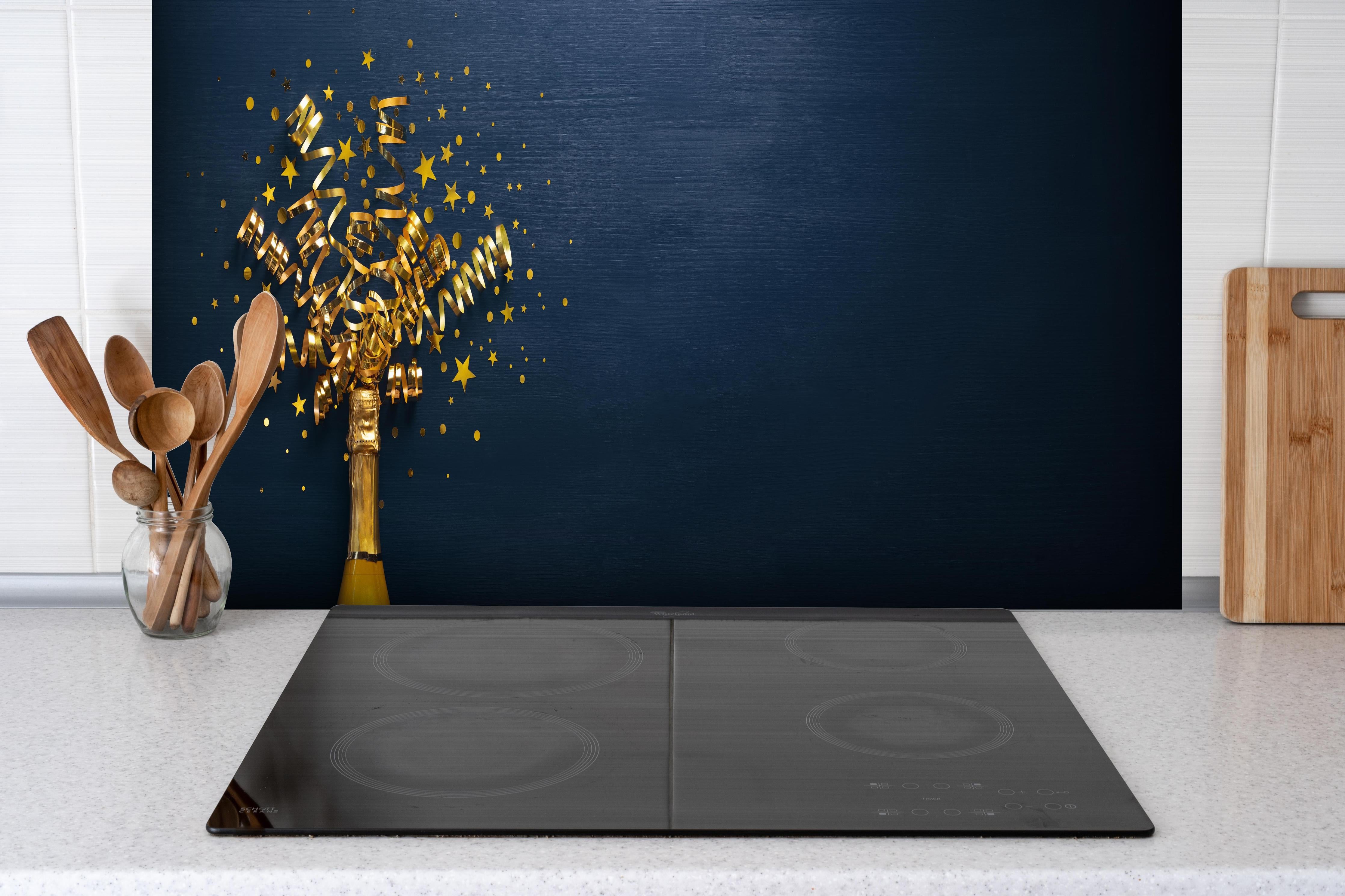 Spritzschutz - Goldene Neujahrsfeier mit Champagner hinter einem Cerankochfeld zwischen Holz-Kochutensilien
