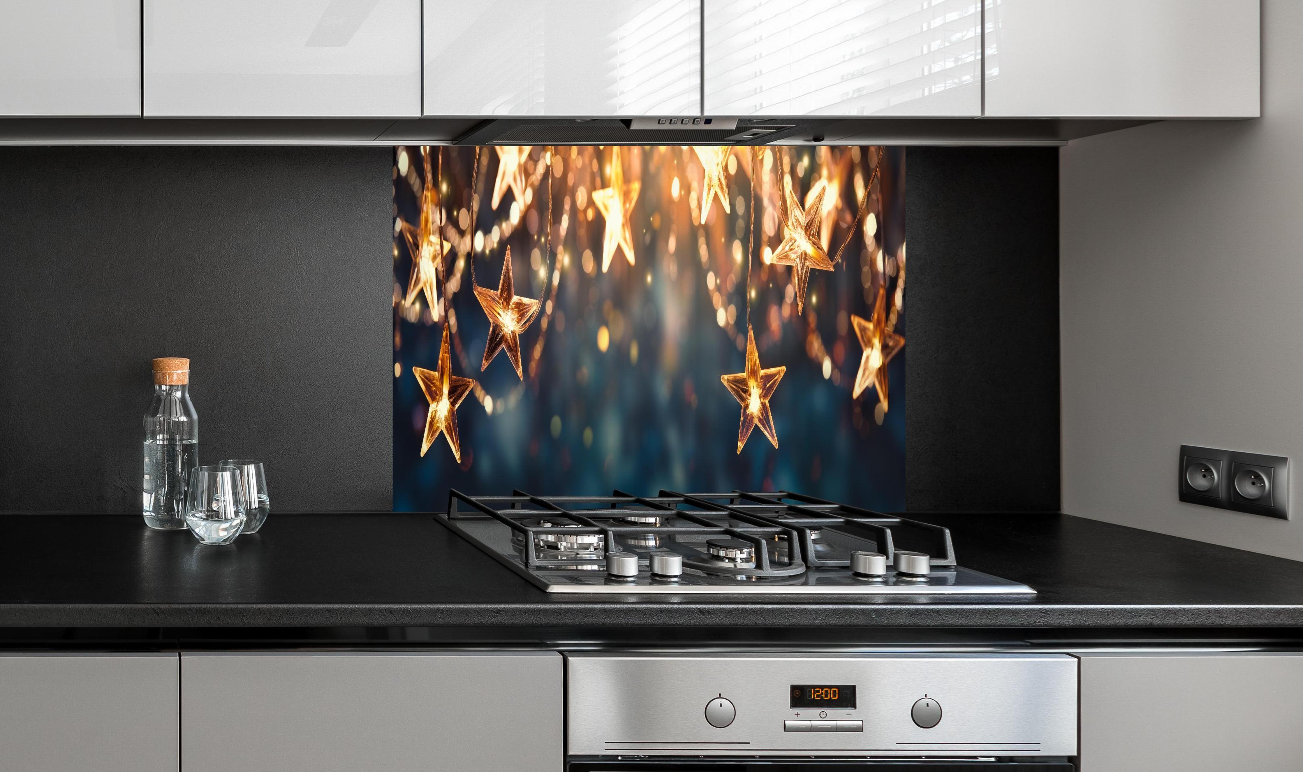 Spritzschutz - Goldene Sternen Lichterkette hinter einem Cerankochfeld zwischen Holz-Kochutensilien
