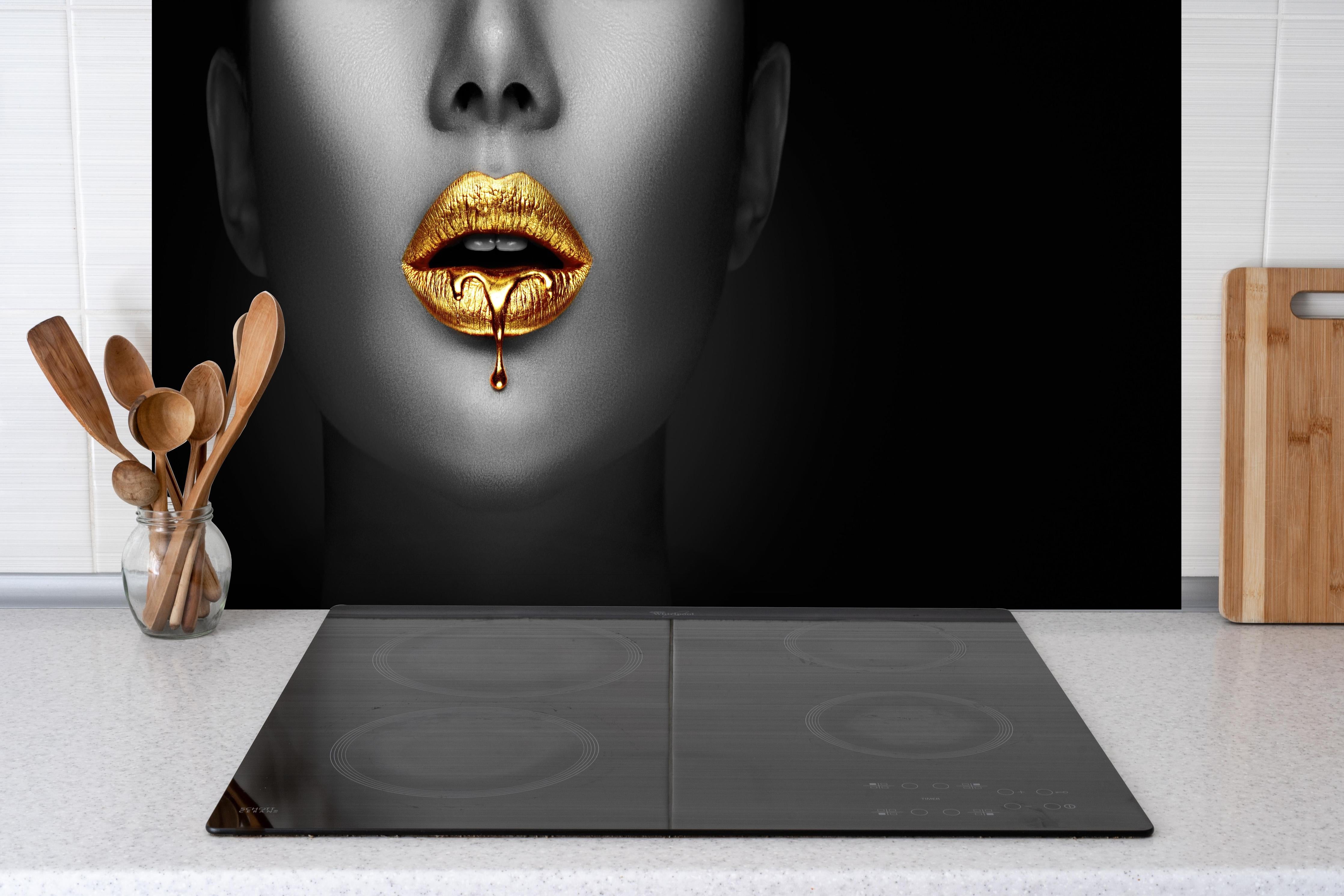 Spritzschutz - Goldener Lipgloss auf sexy Lippen Kunst hinter einem Cerankochfeld zwischen Holz-Kochutensilien
