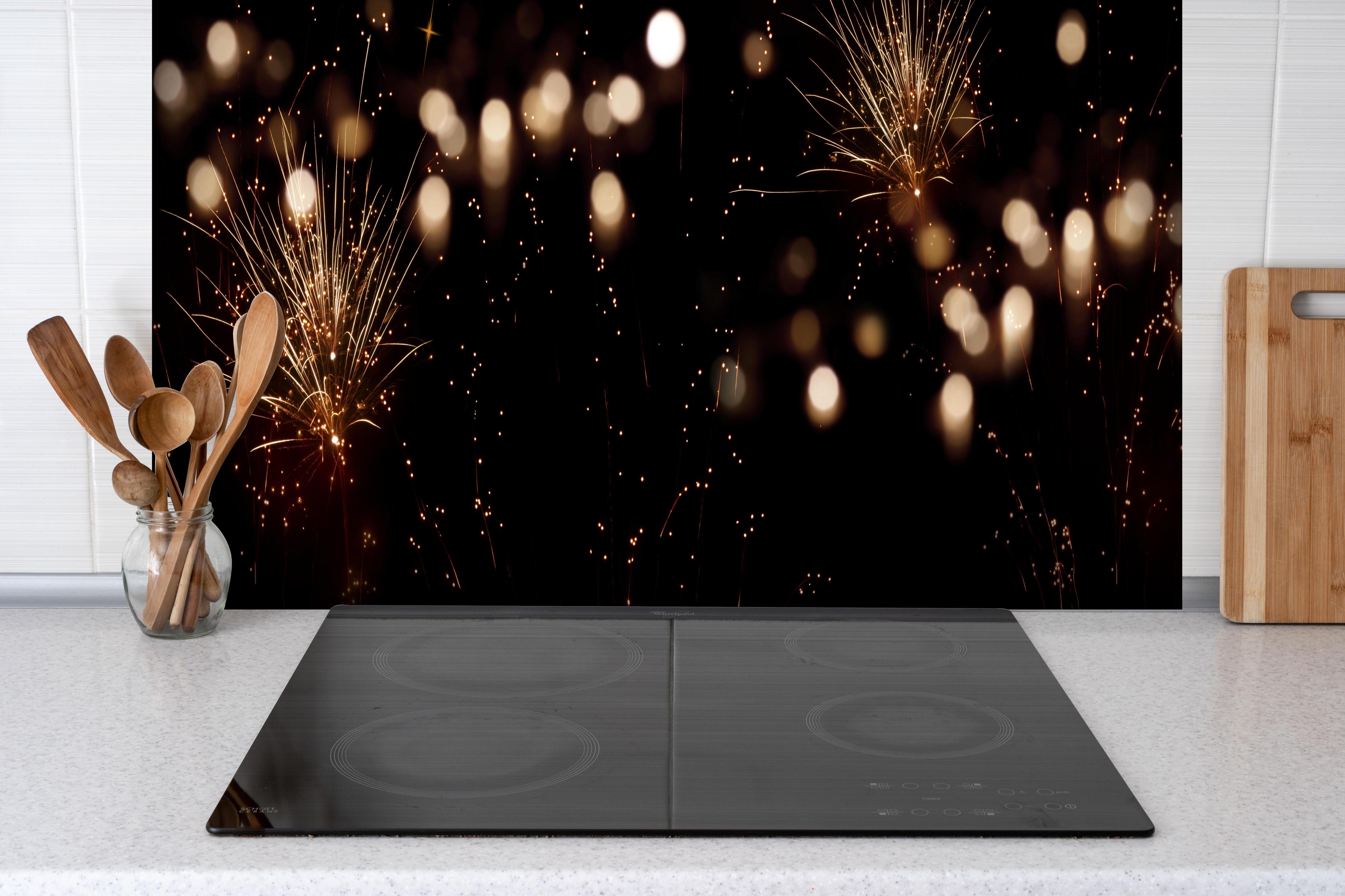 Spritzschutz - Goldenes Feuerwerk am Nachthimmel hinter einem Cerankochfeld zwischen Holz-Kochutensilien
