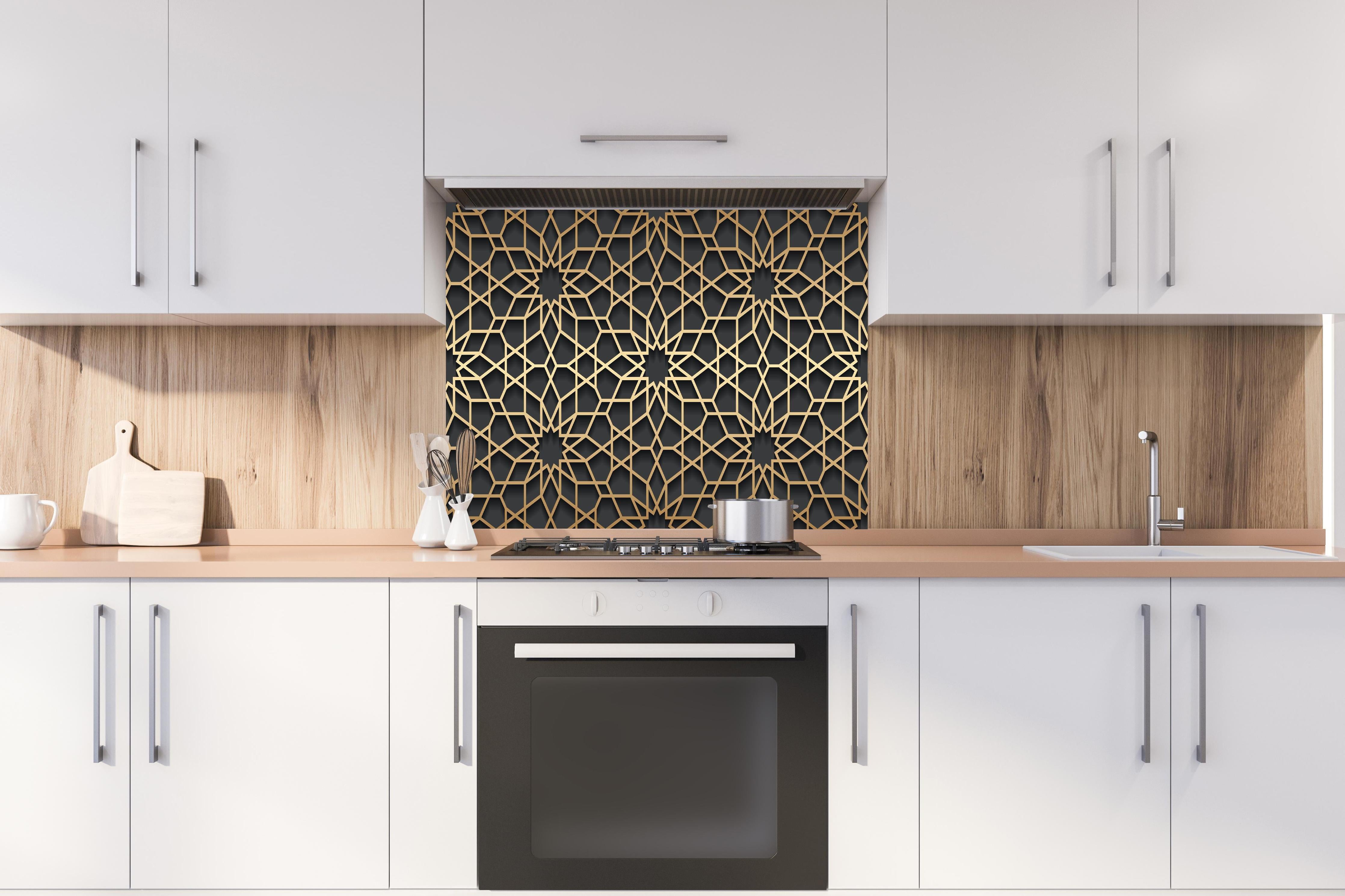 Spritzschutz - Goldenes Muster auf dunklem Hintergrund hinter einem Cerankochfeld zwischen Holz-Kochutensilien
