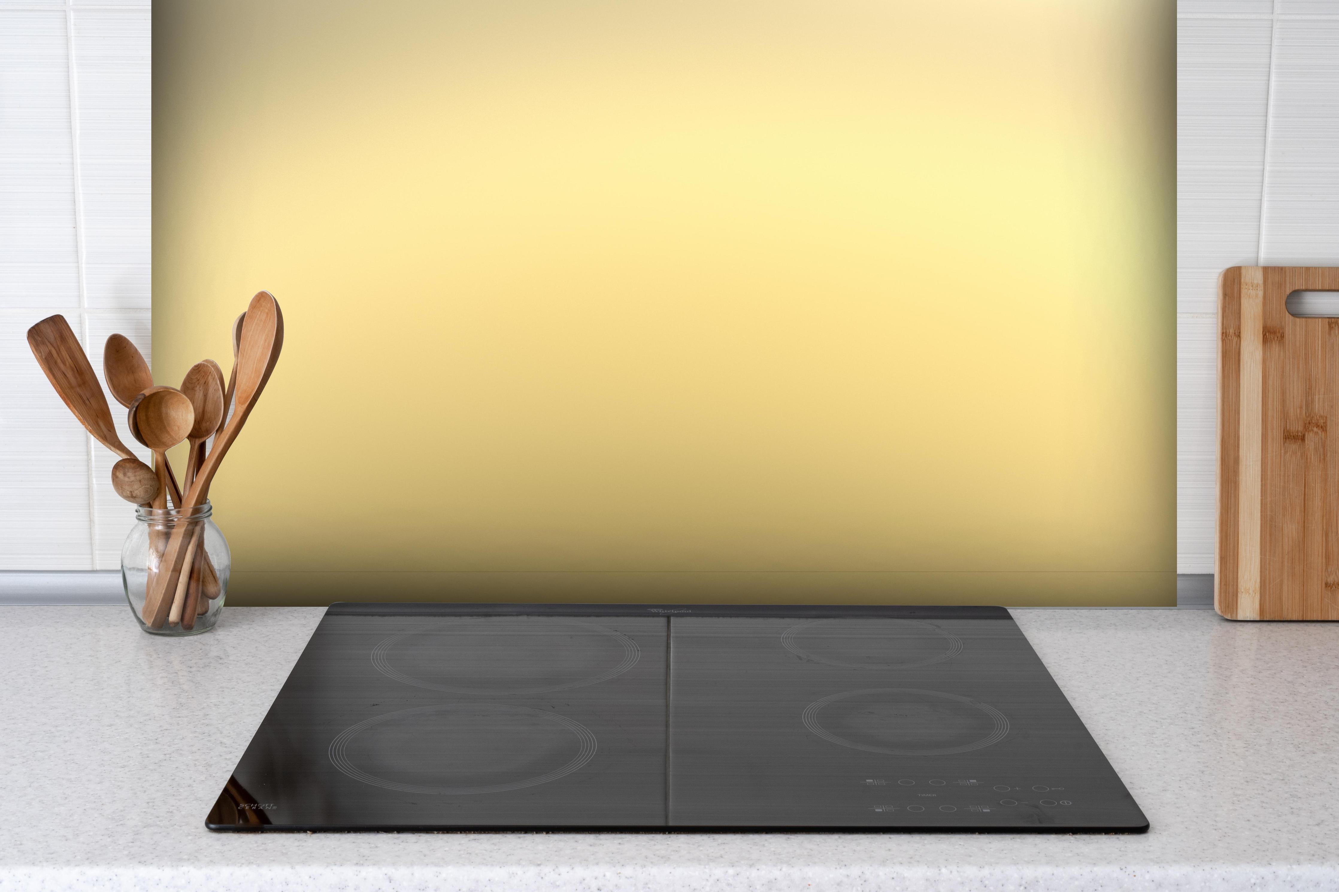 Spritzschutz - Goldenes poliertes Metall hinter einem Cerankochfeld zwischen Holz-Kochutensilien
