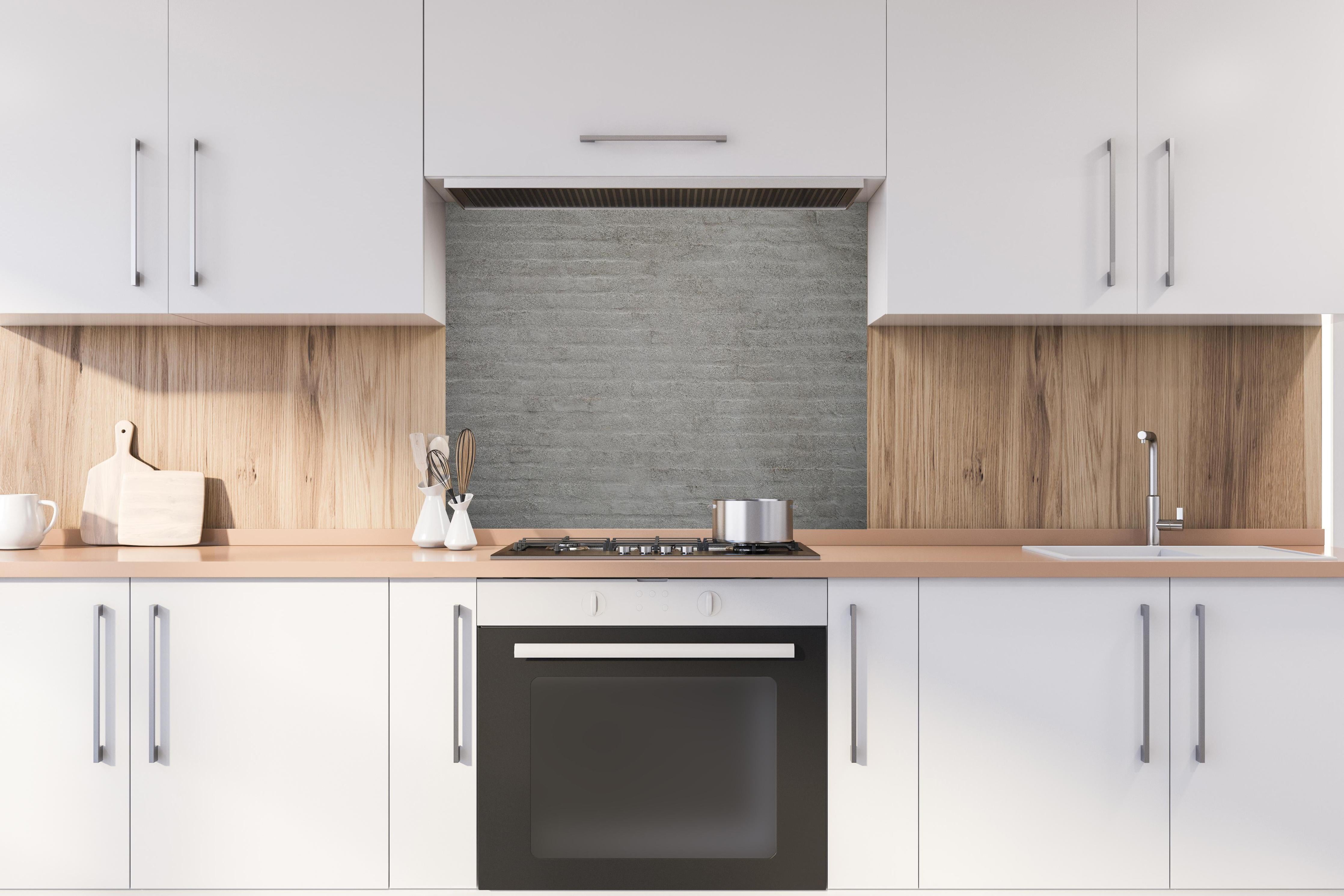 Spritzschutz - Gräuliches Mauerwerk hinter einem Cerankochfeld zwischen Holz-Kochutensilien
