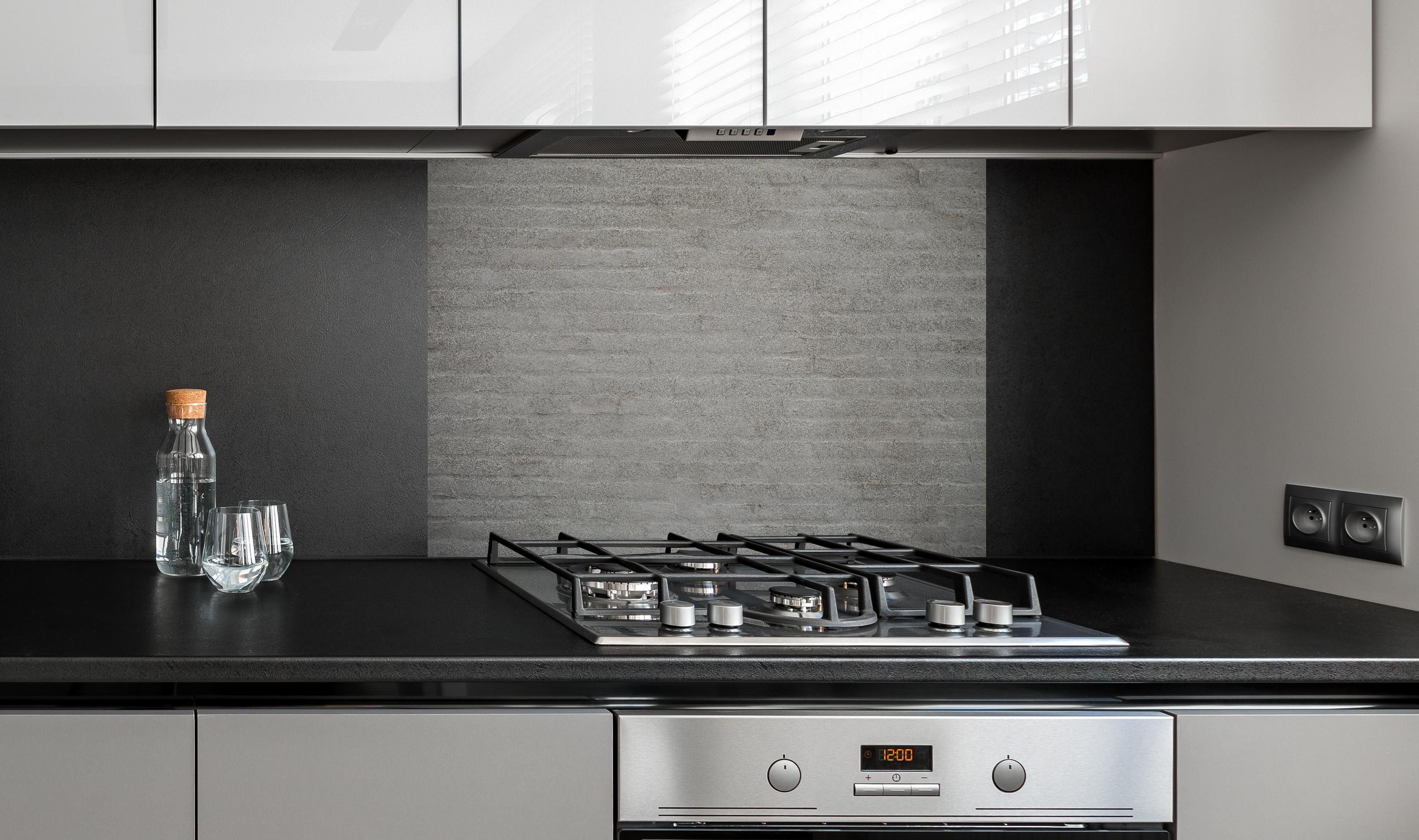 Spritzschutz - Gräuliches Mauerwerk hinter einem Cerankochfeld zwischen Holz-Kochutensilien
