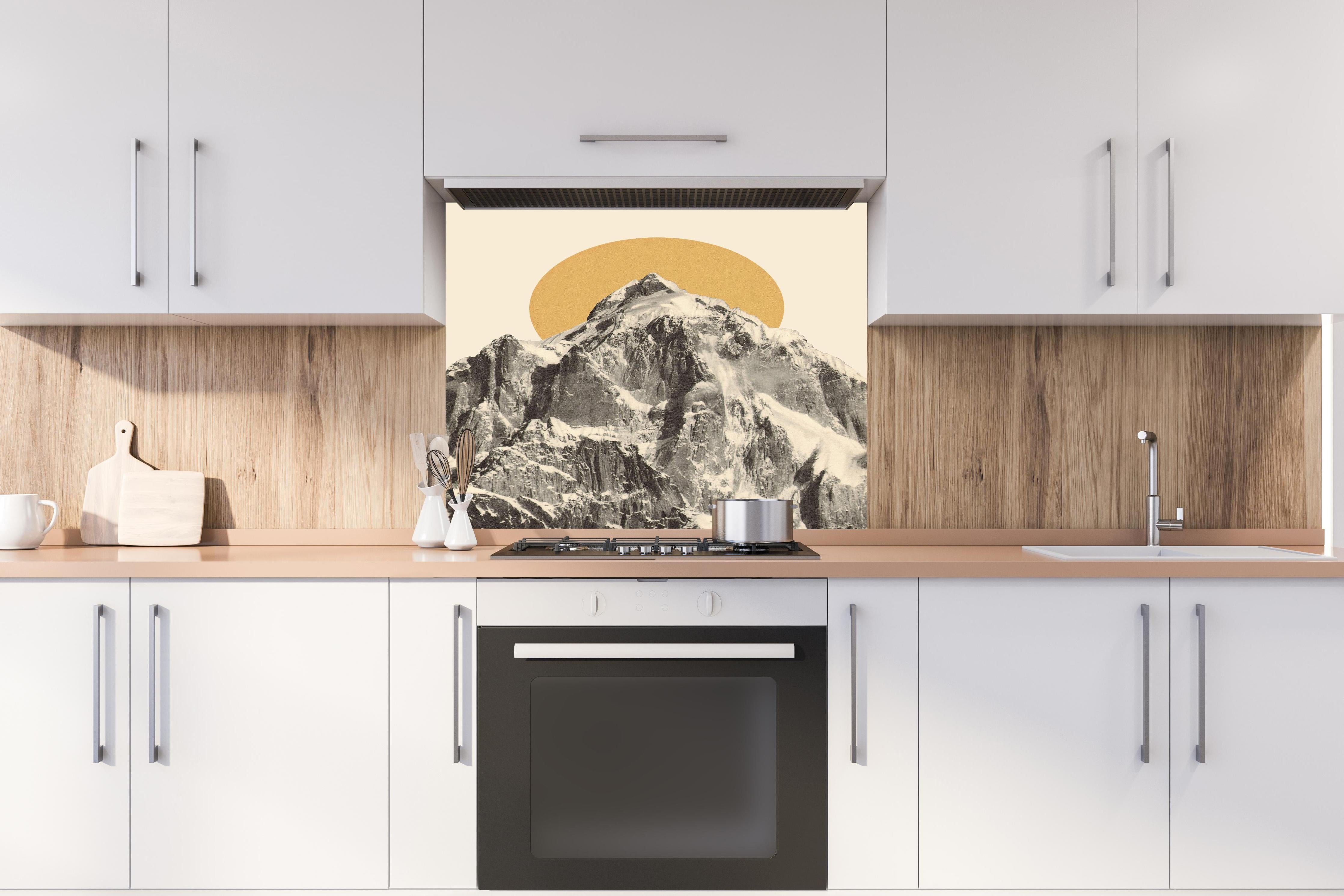Spritzschutz - Grafisches Bergmotiv mit Sonne im Hintergrund hinter einem Cerankochfeld zwischen Holz-Kochutensilien

