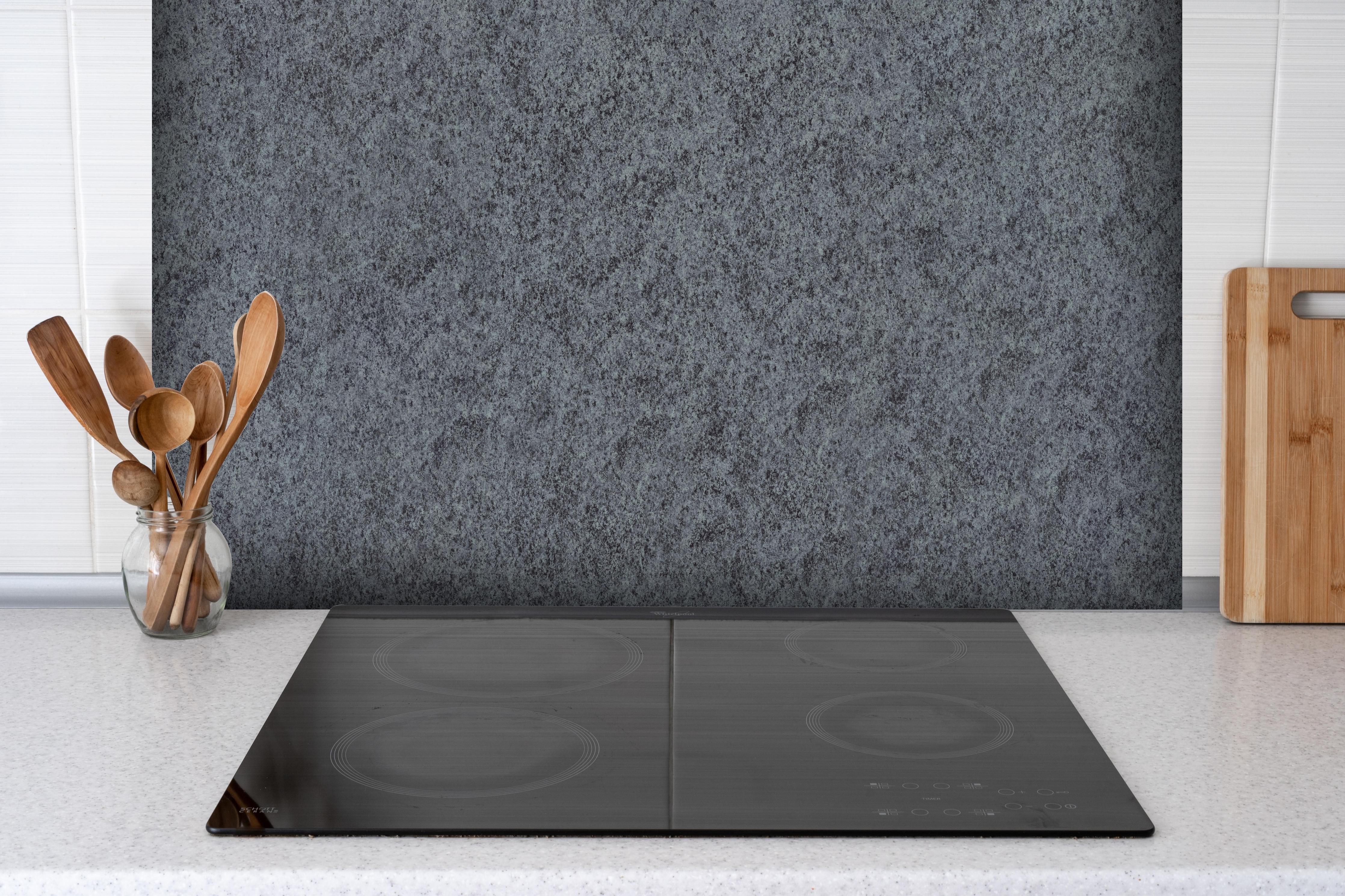 Spritzschutz - Granit Marmor Textur hinter einem Cerankochfeld zwischen Holz-Kochutensilien
