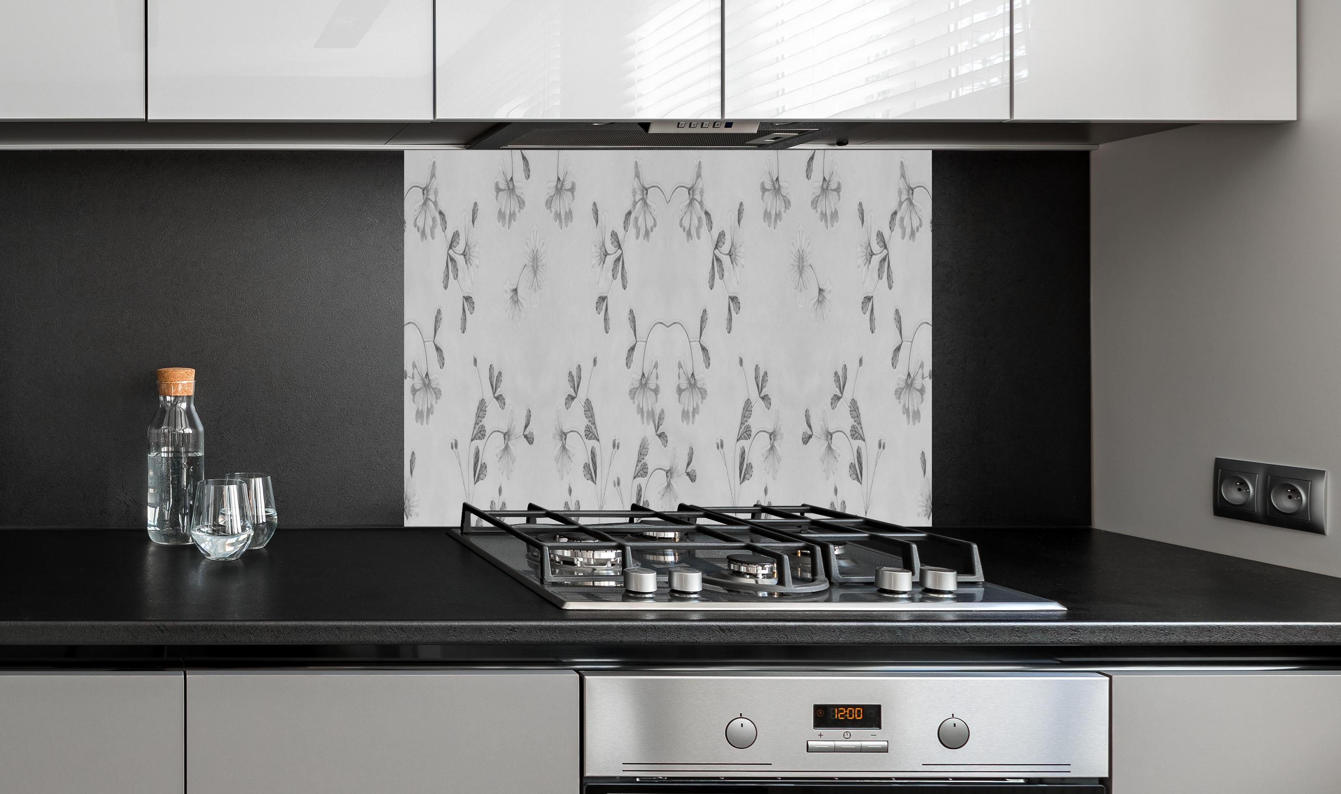 Spritzschutz - Grau-Weißes Blumenmuster auf Textil hinter einem Cerankochfeld zwischen Holz-Kochutensilien
