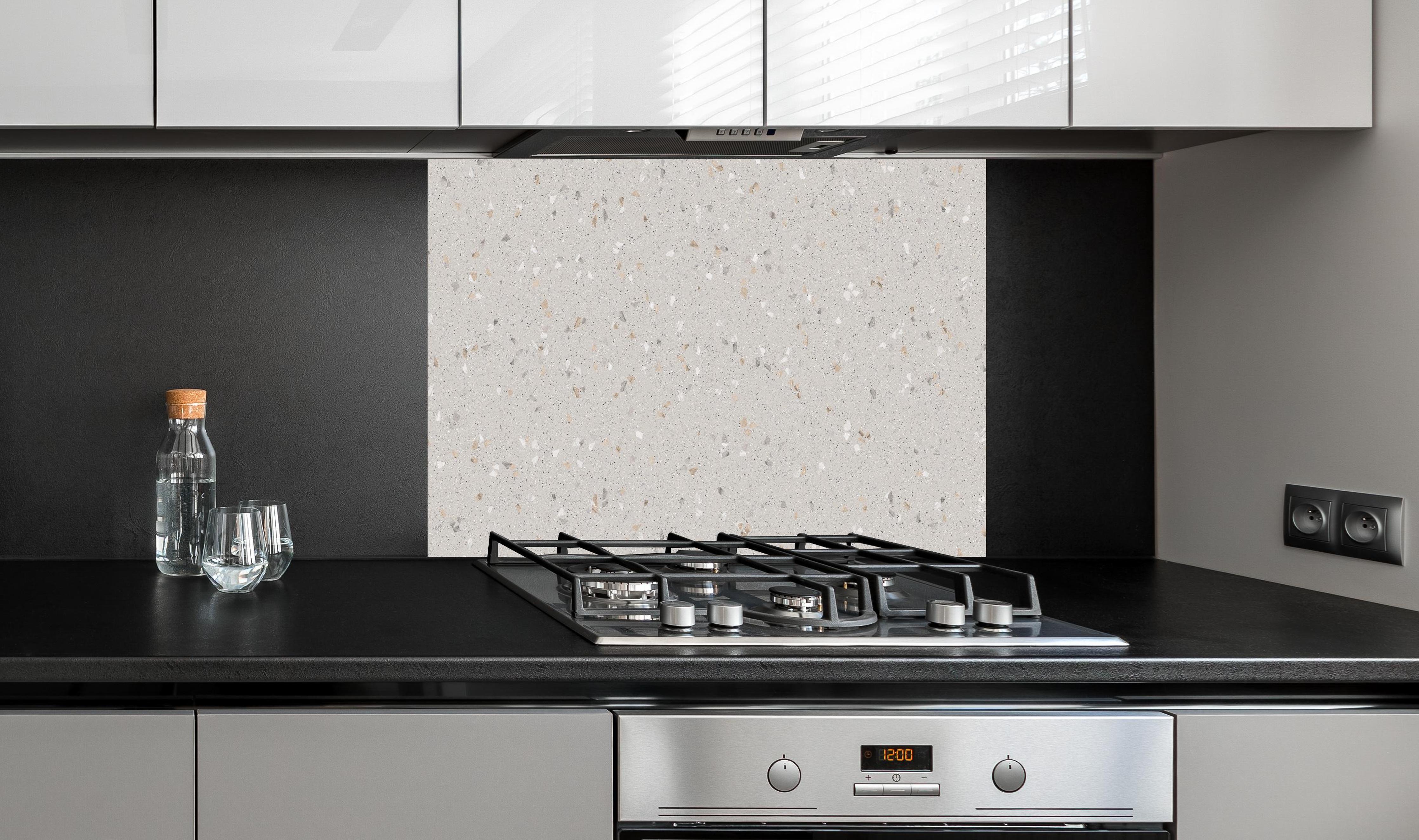 Spritzschutz - Graue Mosaiksteine  hinter einem Cerankochfeld zwischen Holz-Kochutensilien
