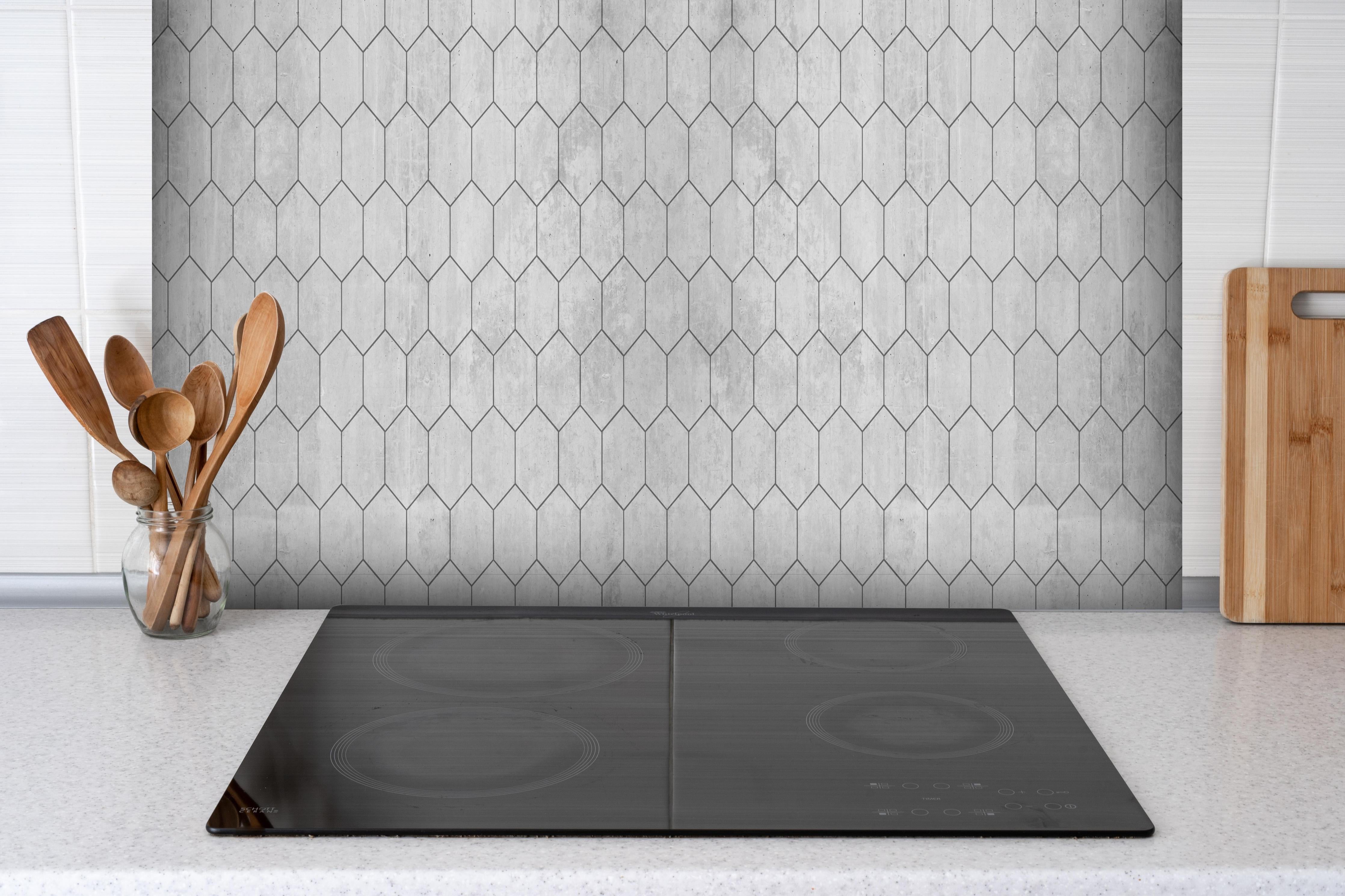 Spritzschutz - Graue sechseckige Mustern hinter einem Cerankochfeld zwischen Holz-Kochutensilien
