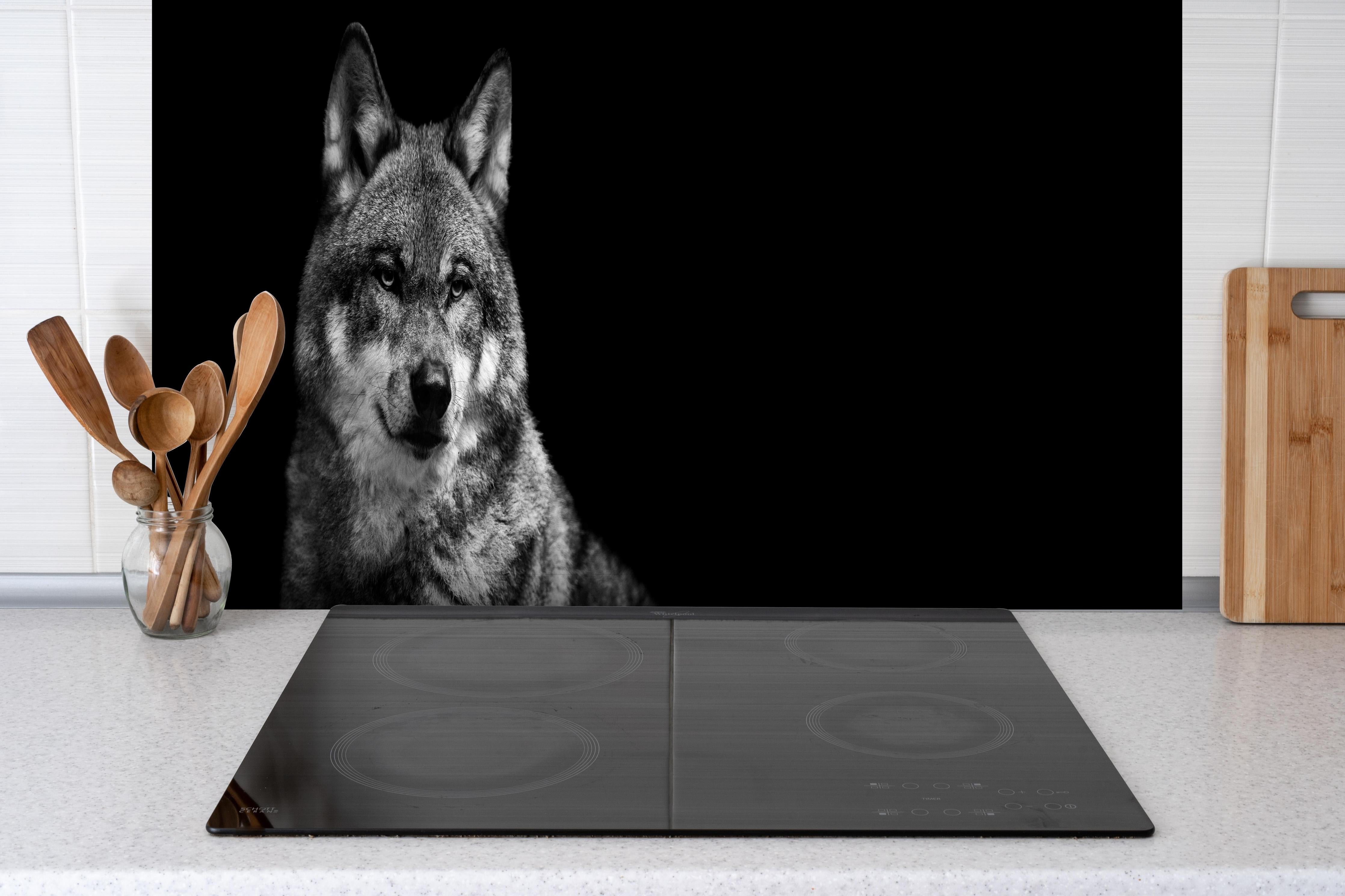 Spritzschutz - Grauer Wolf auf schwarzem Hintergrund hinter einem Cerankochfeld zwischen Holz-Kochutensilien
