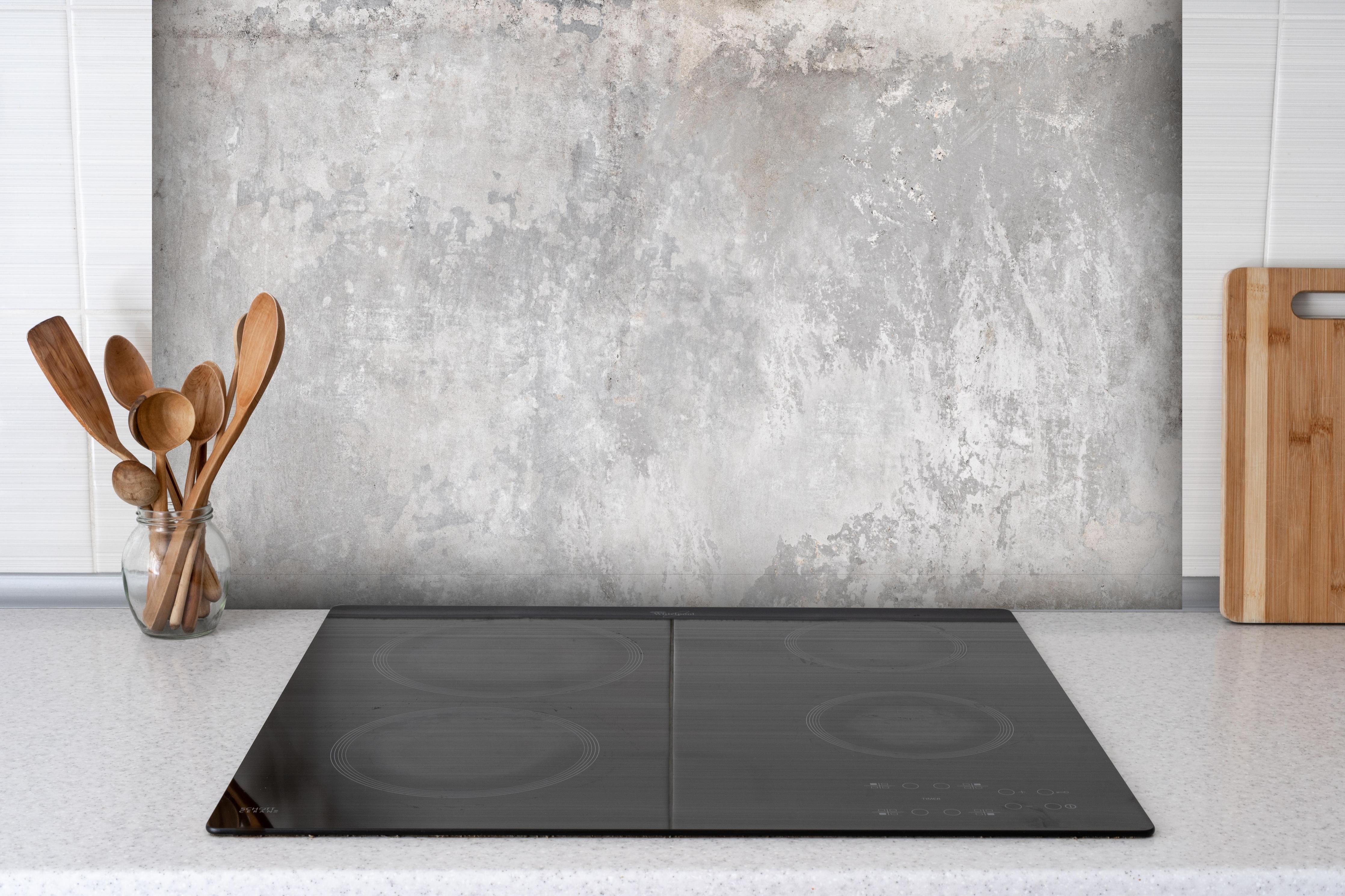 Spritzschutz - Grauer Zement-Hintergrund hinter einem Cerankochfeld zwischen Holz-Kochutensilien
