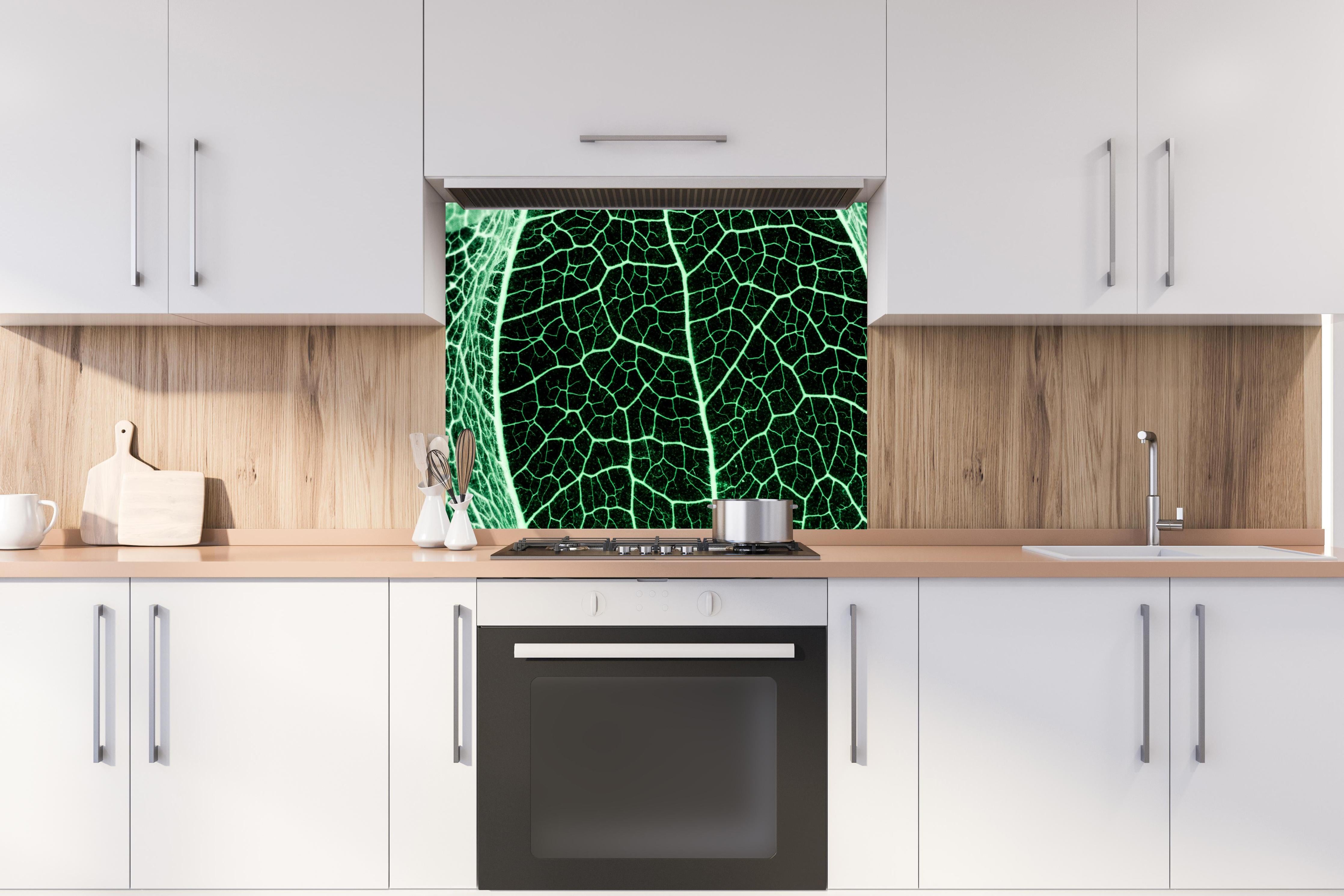 Spritzschutz - Grünliche Blatttextur im Detail hinter einem Cerankochfeld zwischen Holz-Kochutensilien
