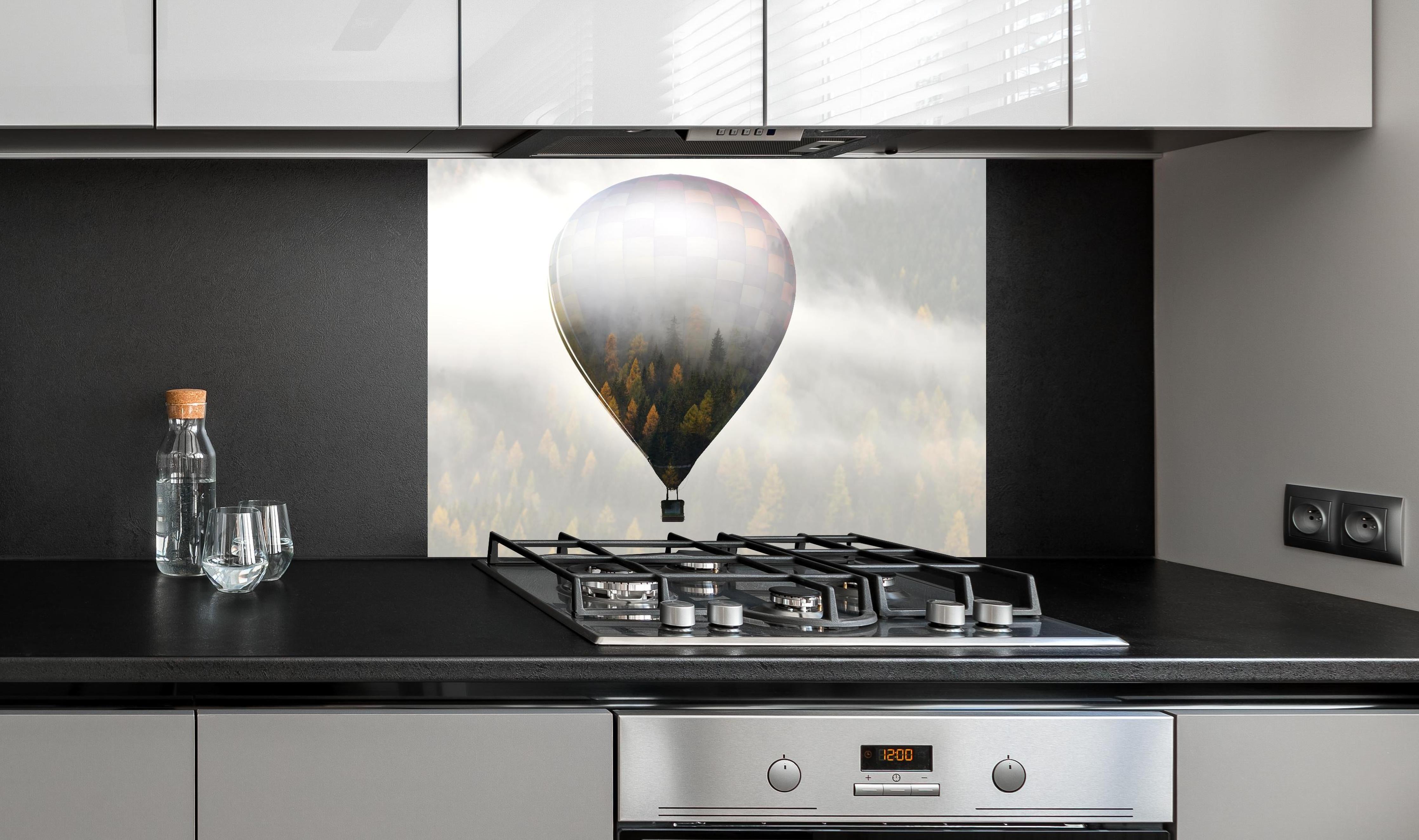 Spritzschutz - Heißluftballon - Spiegelung des Waldes hinter einem Cerankochfeld zwischen Holz-Kochutensilien
