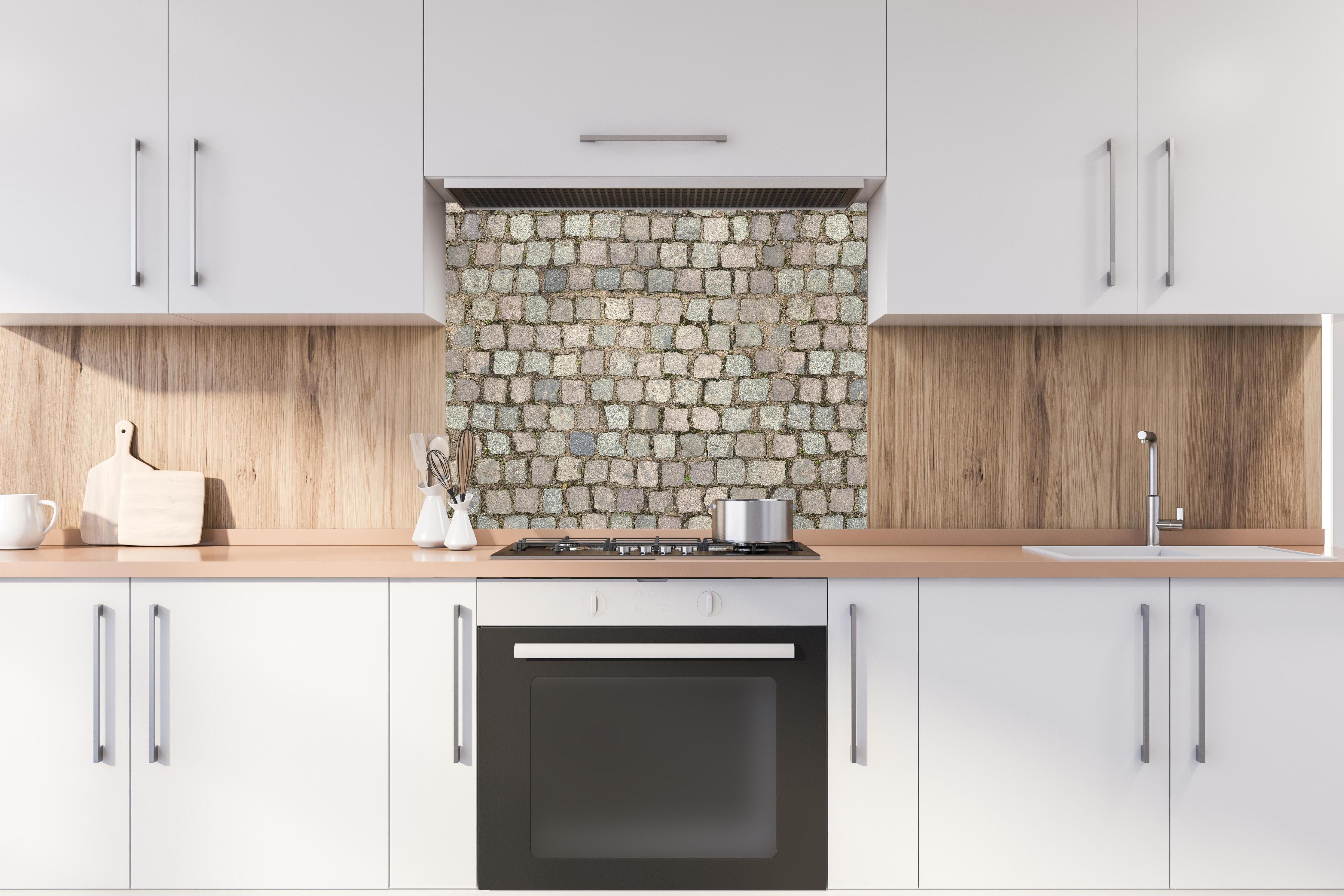 Spritzschutz - Historisches Grau-Braunes Kopfsteinpflaster hinter einem Cerankochfeld zwischen Holz-Kochutensilien
