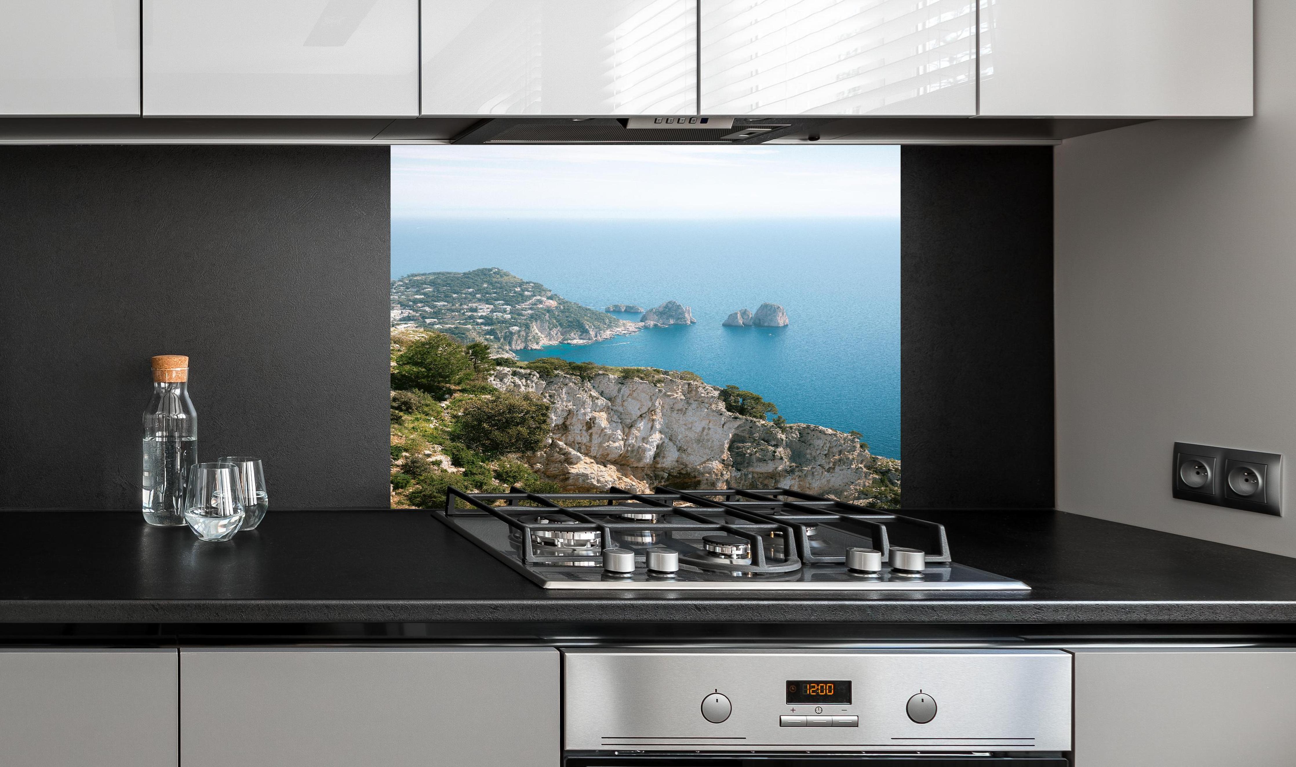 Spritzschutz - Idyllische Capri Küste und blaues Meer hinter einem Cerankochfeld zwischen Holz-Kochutensilien
