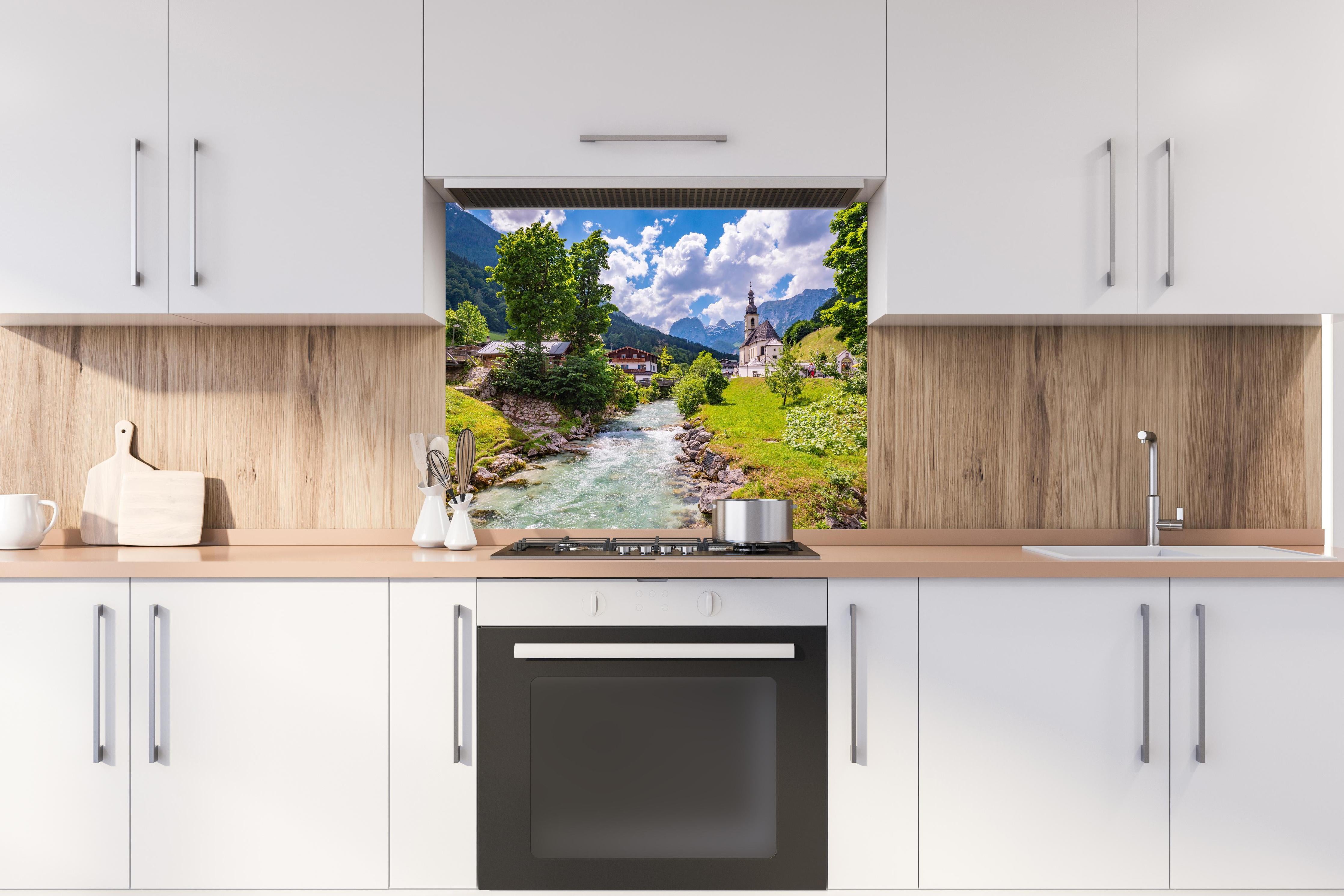 Spritzschutz - Idyllische Ramsau Kirche mit Bergblick hinter einem Cerankochfeld zwischen Holz-Kochutensilien
