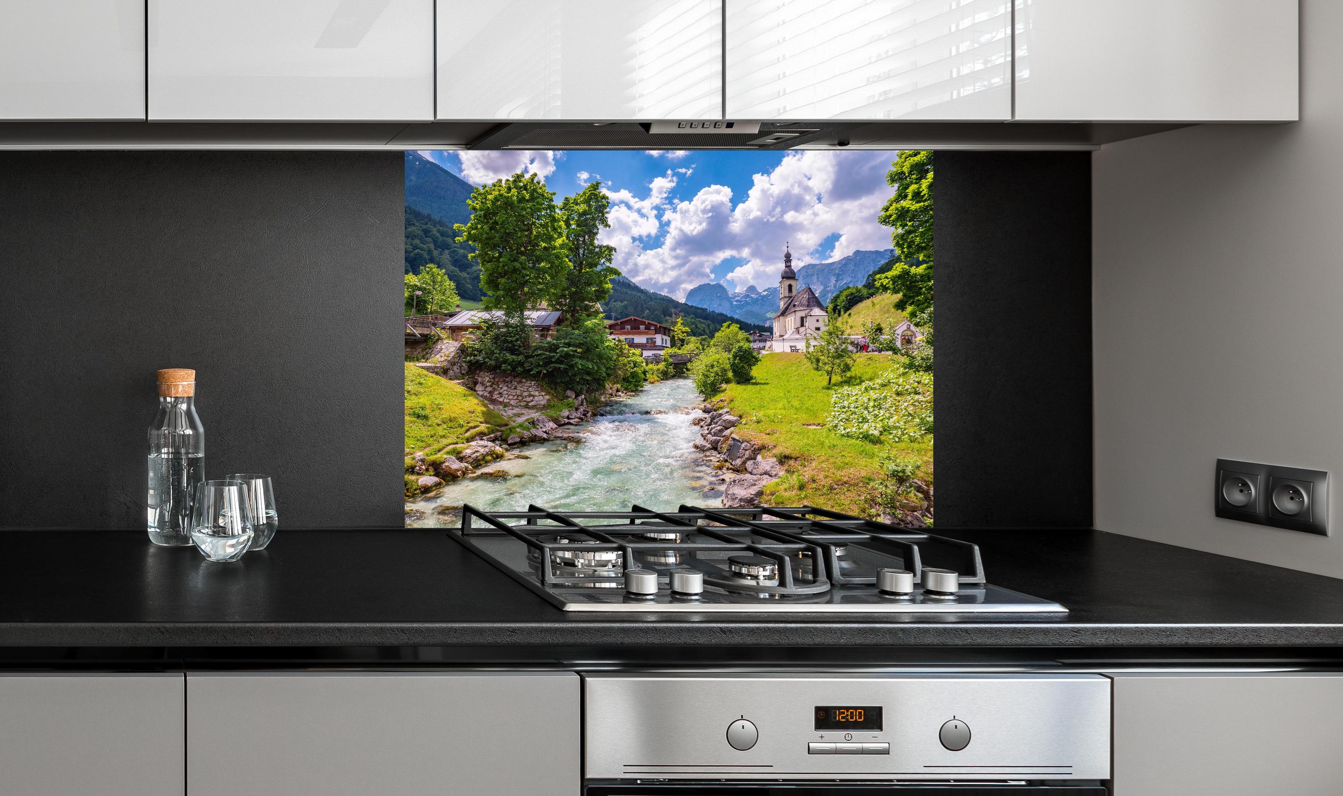 Spritzschutz - Idyllische Ramsau Kirche mit Bergblick hinter einem Cerankochfeld zwischen Holz-Kochutensilien
