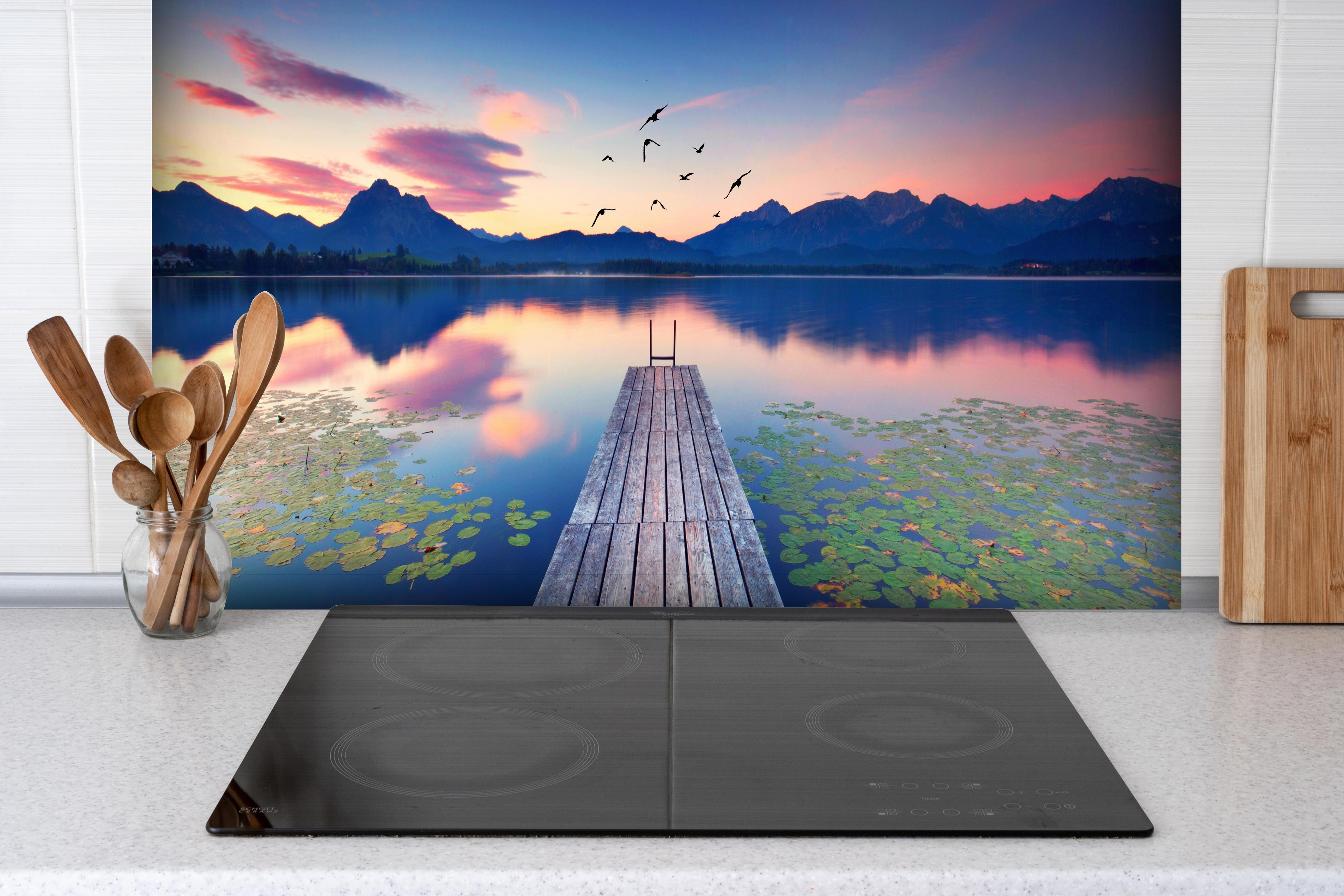 Spritzschutz - Idyllischer Alpensee Sonnenuntergang Seerosen hinter einem Cerankochfeld zwischen Holz-Kochutensilien
