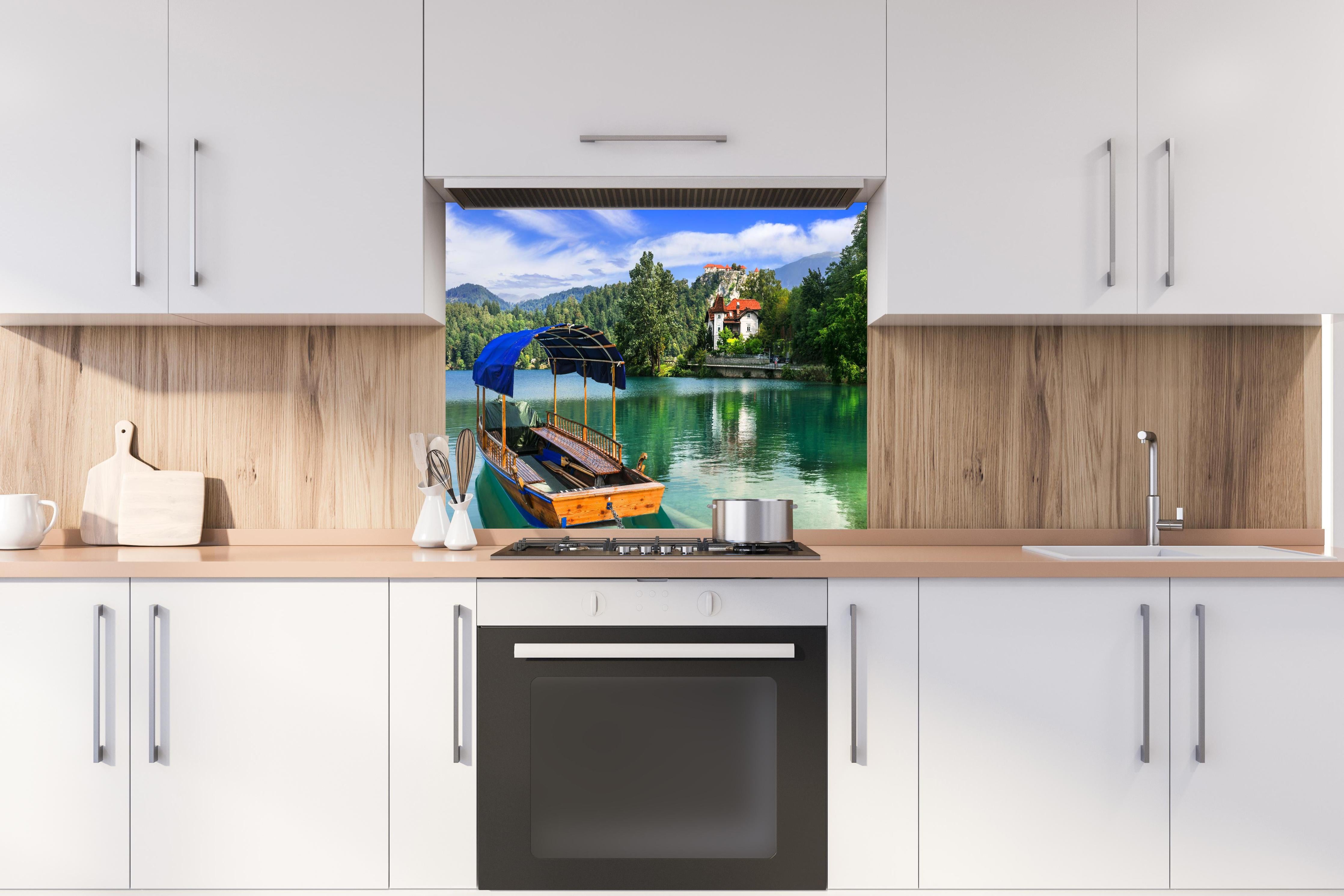 Spritzschutz - Idyllischer Bled See, Holzboot, Slowenien hinter einem Cerankochfeld zwischen Holz-Kochutensilien
