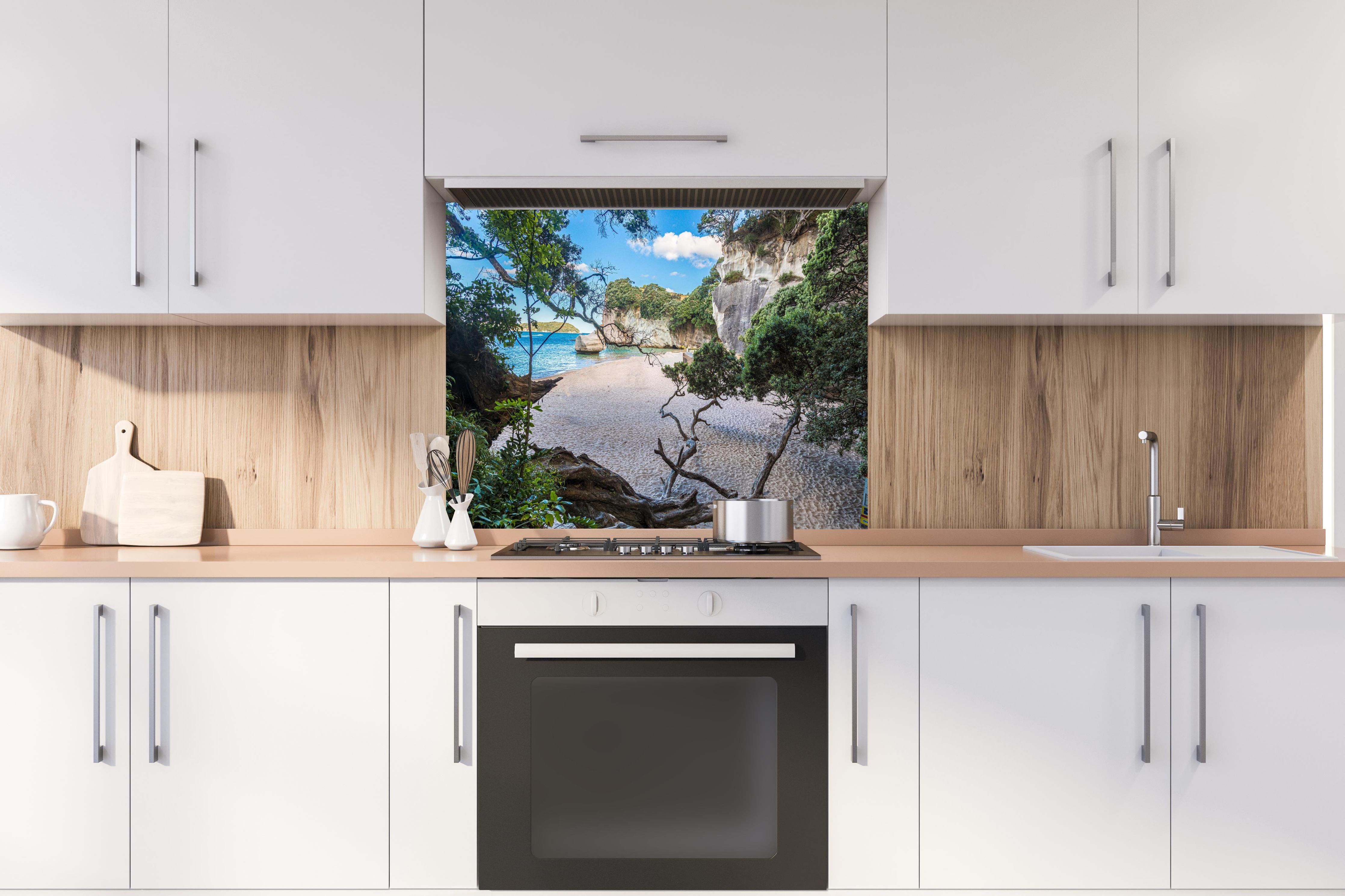 Spritzschutz - Idyllischer Sommerstrand Cathedral Cove hinter einem Cerankochfeld zwischen Holz-Kochutensilien
