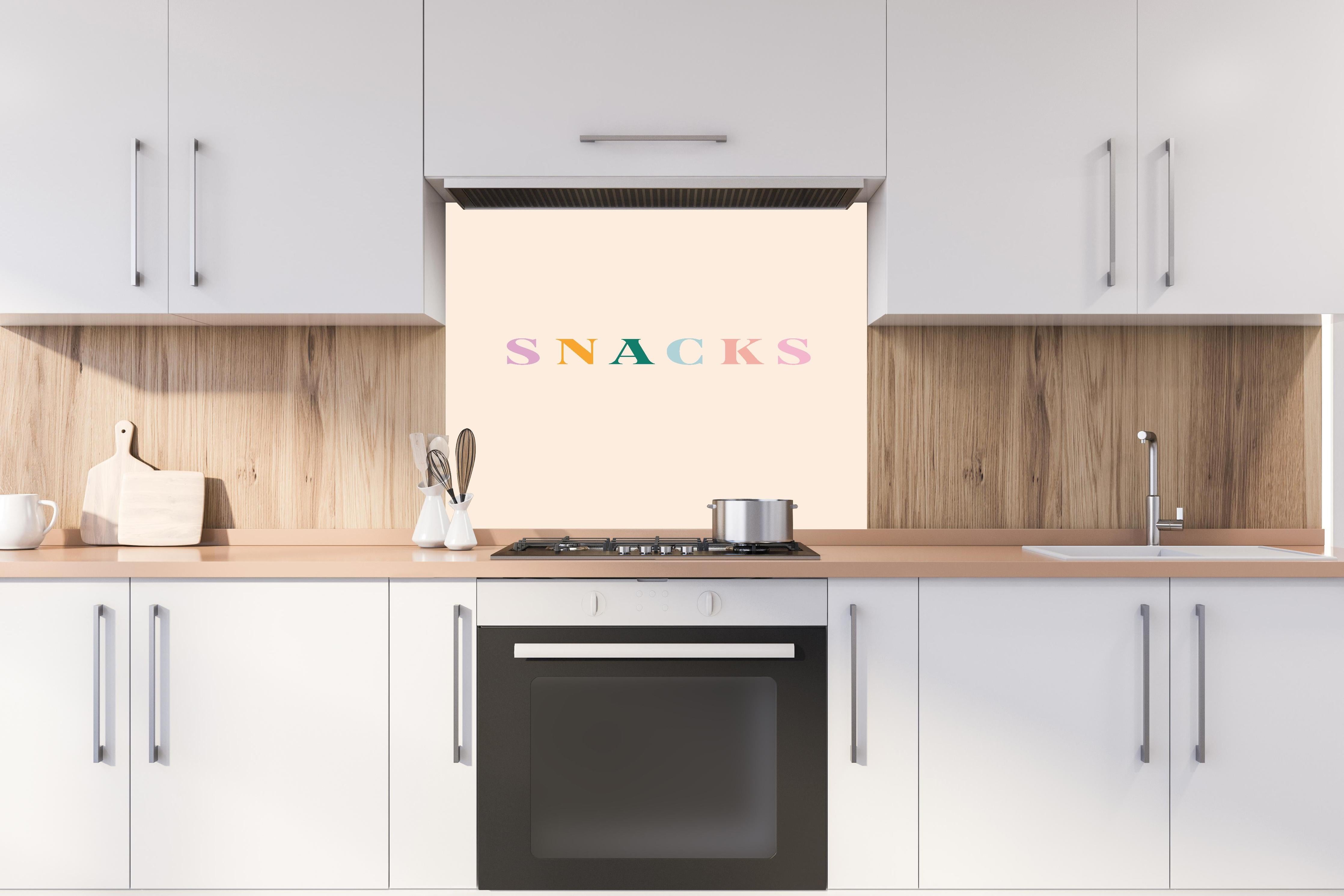 Spritzschutz - Inspirierende 'SNACKS'-Schrift in Pastellfarben hinter einem Cerankochfeld zwischen Holz-Kochutensilien
