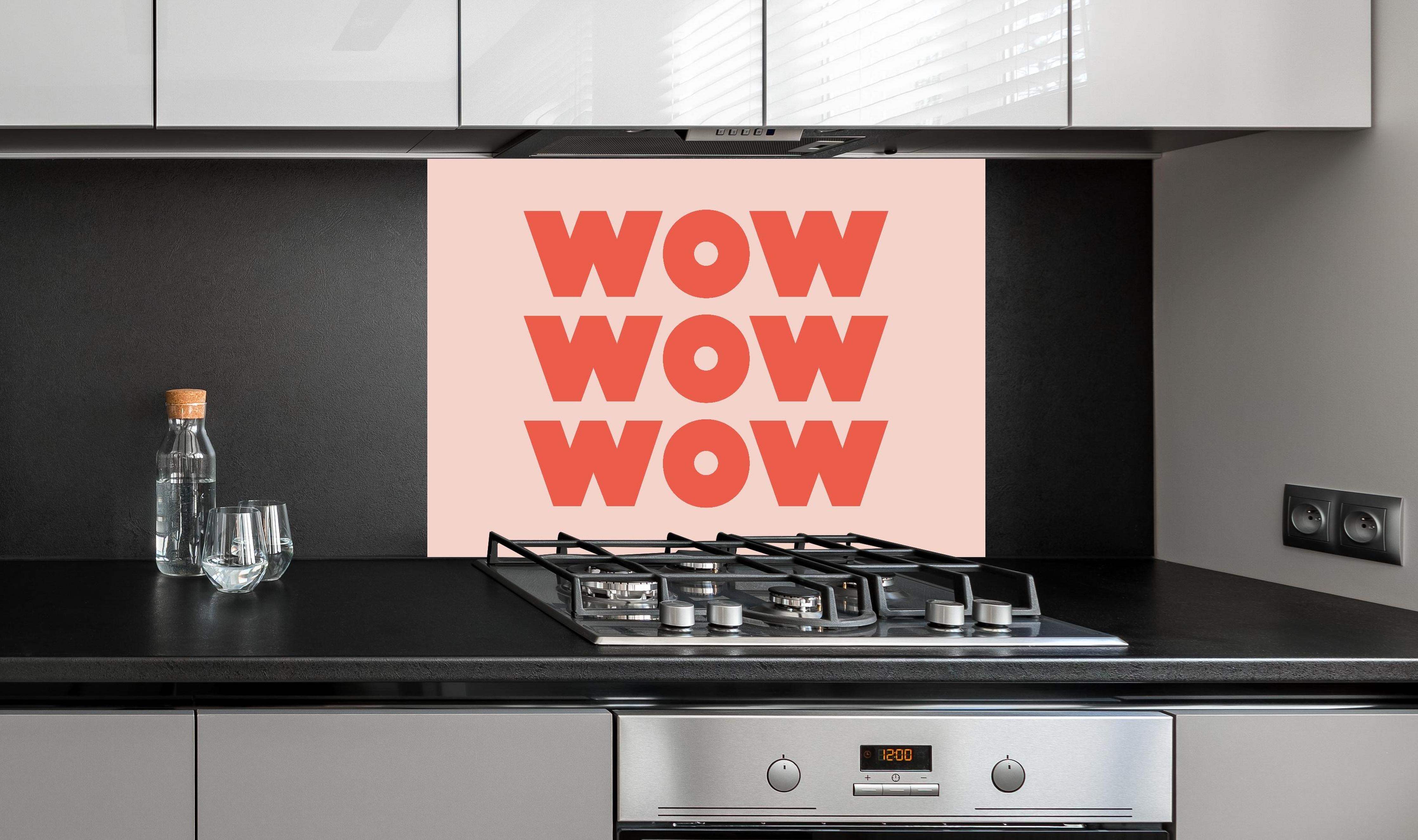 Spritzschutz - Inspirierender 'WOW' Text auf Pinkem Hintergrund hinter einem Cerankochfeld zwischen Holz-Kochutensilien
