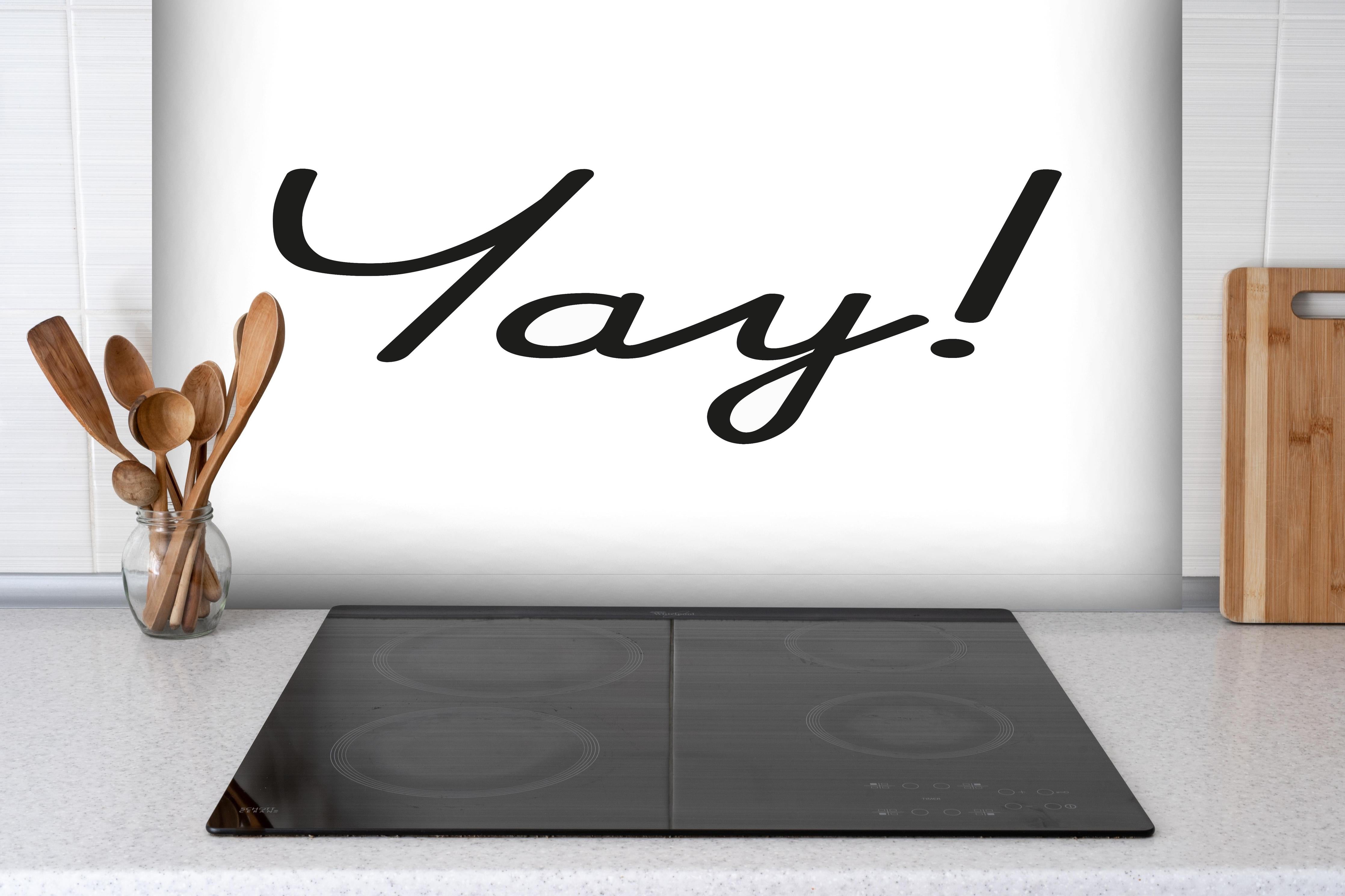 Spritzschutz - Inspirierender 'Yay!' Schriftzug in Schwarz auf Weiß hinter einem Cerankochfeld zwischen Holz-Kochutensilien
