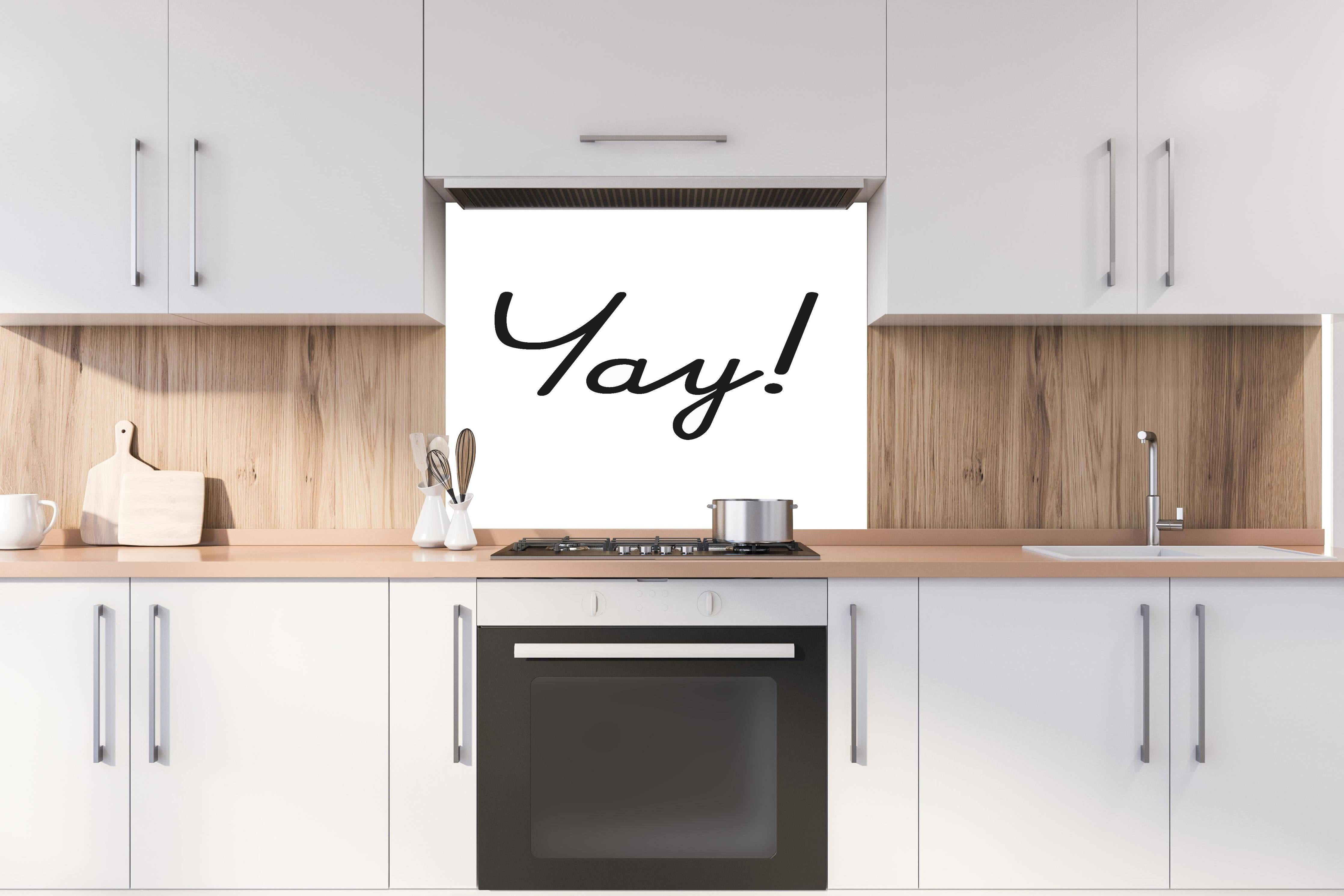 Spritzschutz - Inspirierender 'Yay!' Schriftzug in Schwarz auf Weiß hinter einem Cerankochfeld zwischen Holz-Kochutensilien
