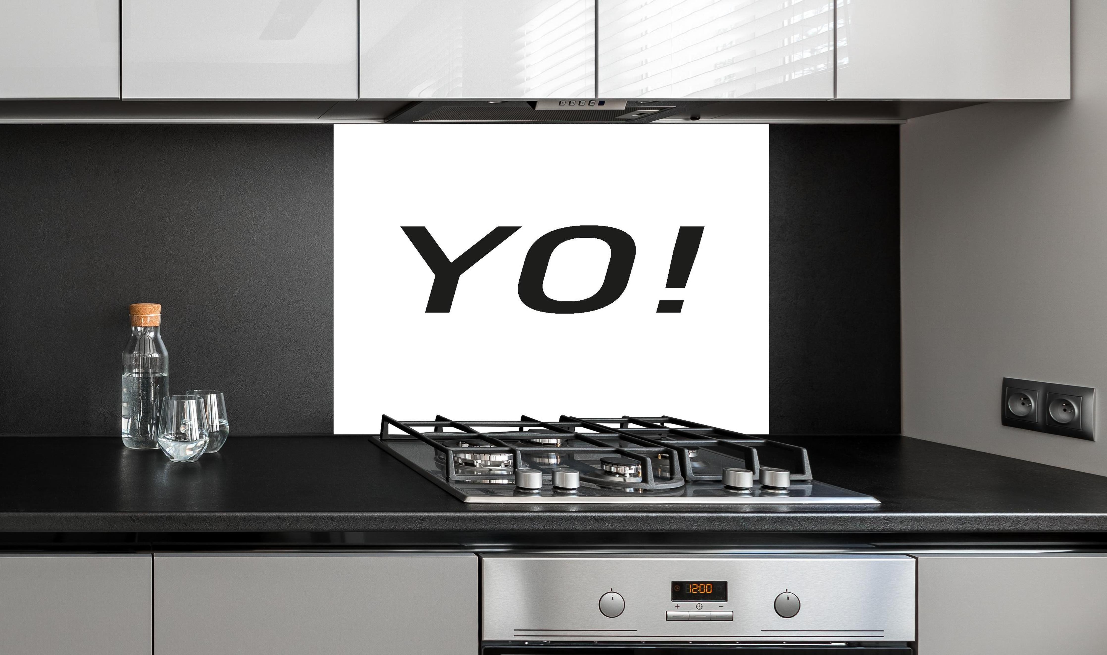 Spritzschutz - Inspirierendes 'YO!' in Schwarz auf Weiß hinter einem Cerankochfeld zwischen Holz-Kochutensilien
