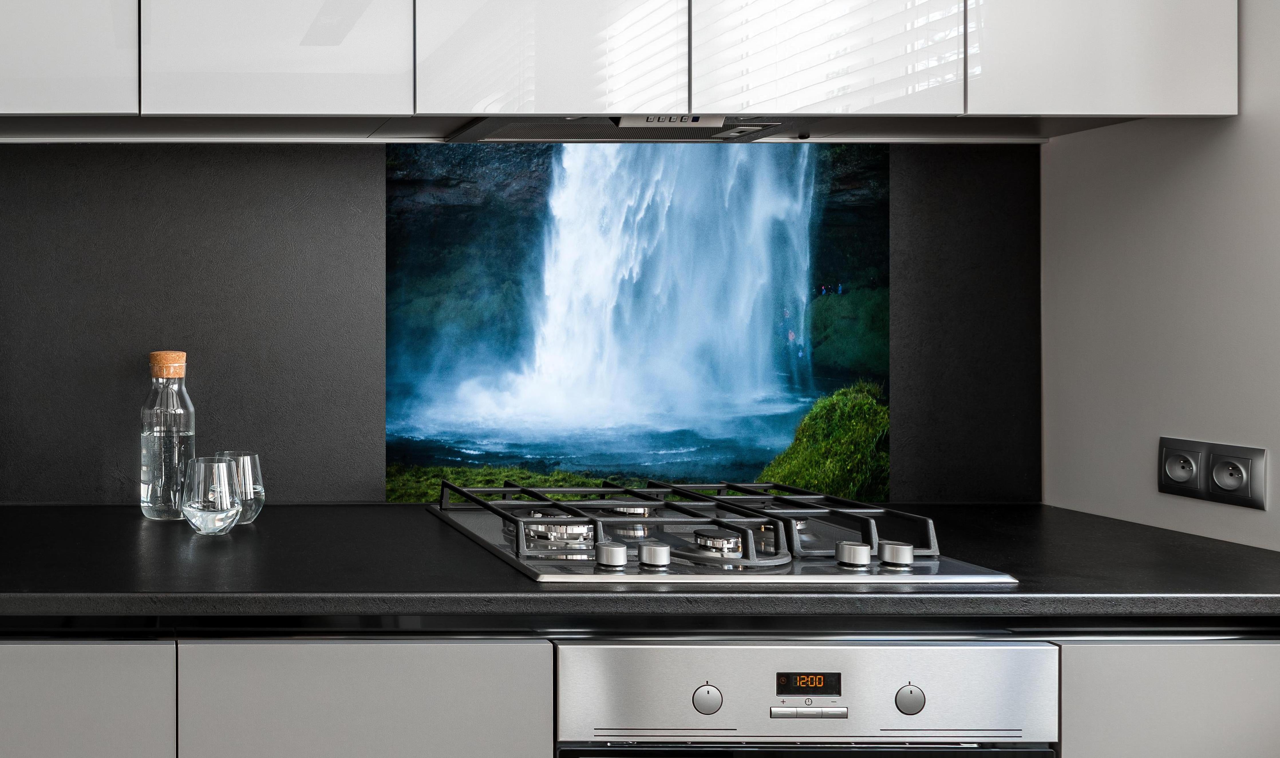 Spritzschutz - Islands beeindruckender Wasserfall in Blau hinter einem Cerankochfeld zwischen Holz-Kochutensilien
