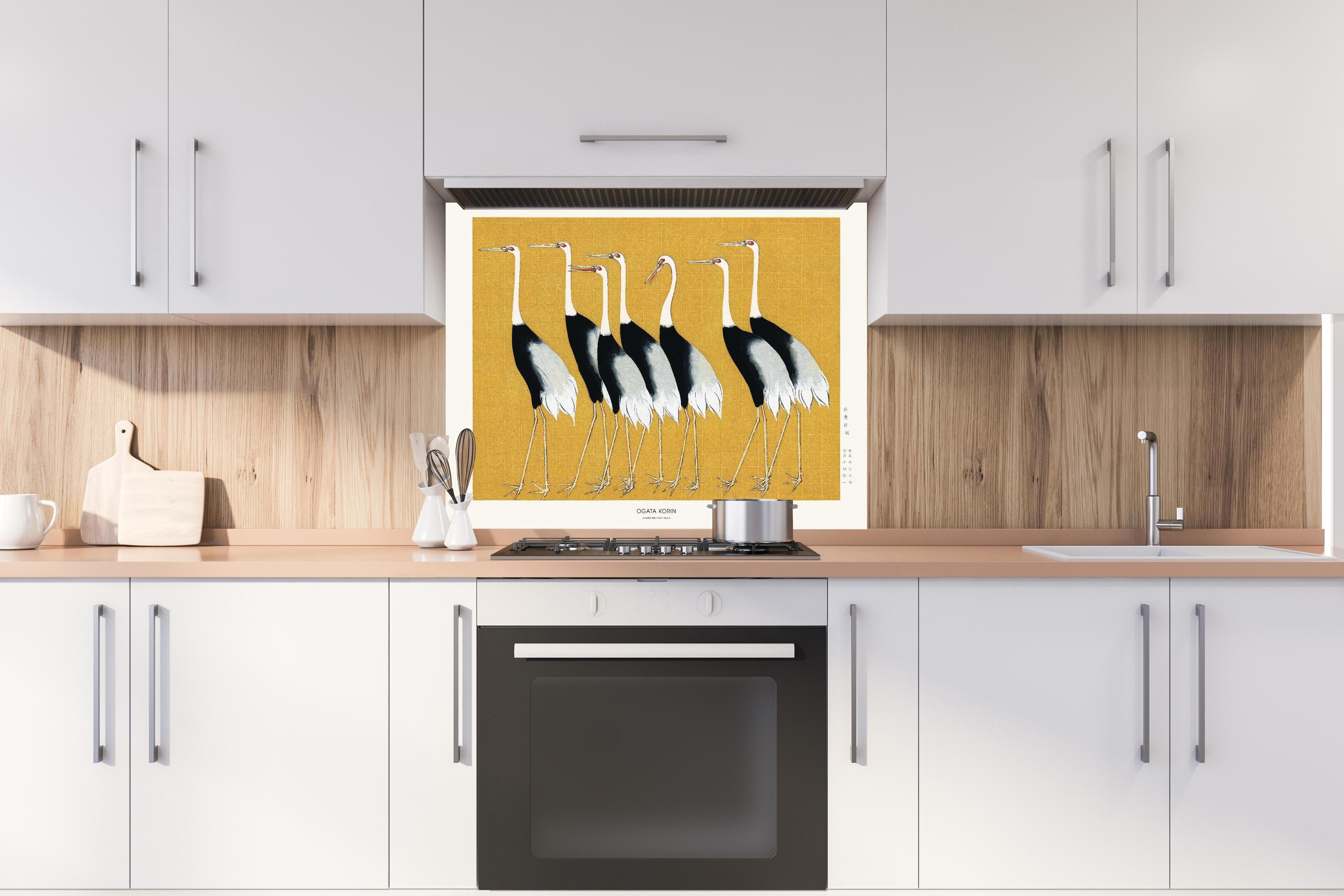 Spritzschutz - Japanischer Mandschurenkranich - Gold hinter einem Cerankochfeld zwischen Holz-Kochutensilien
