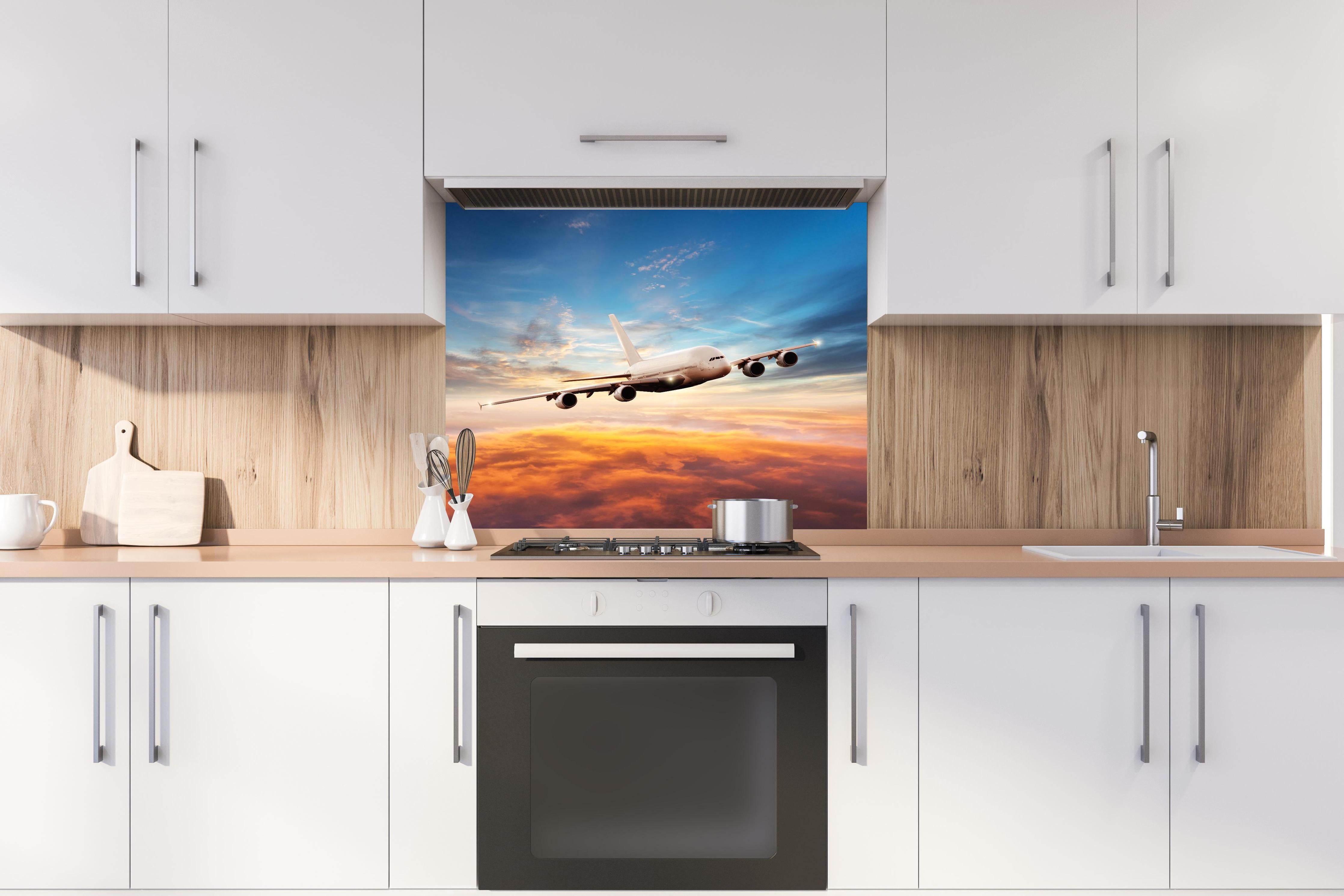 Spritzschutz - Jet im Sonnenuntergang über Wolken hinter einem Cerankochfeld zwischen Holz-Kochutensilien
