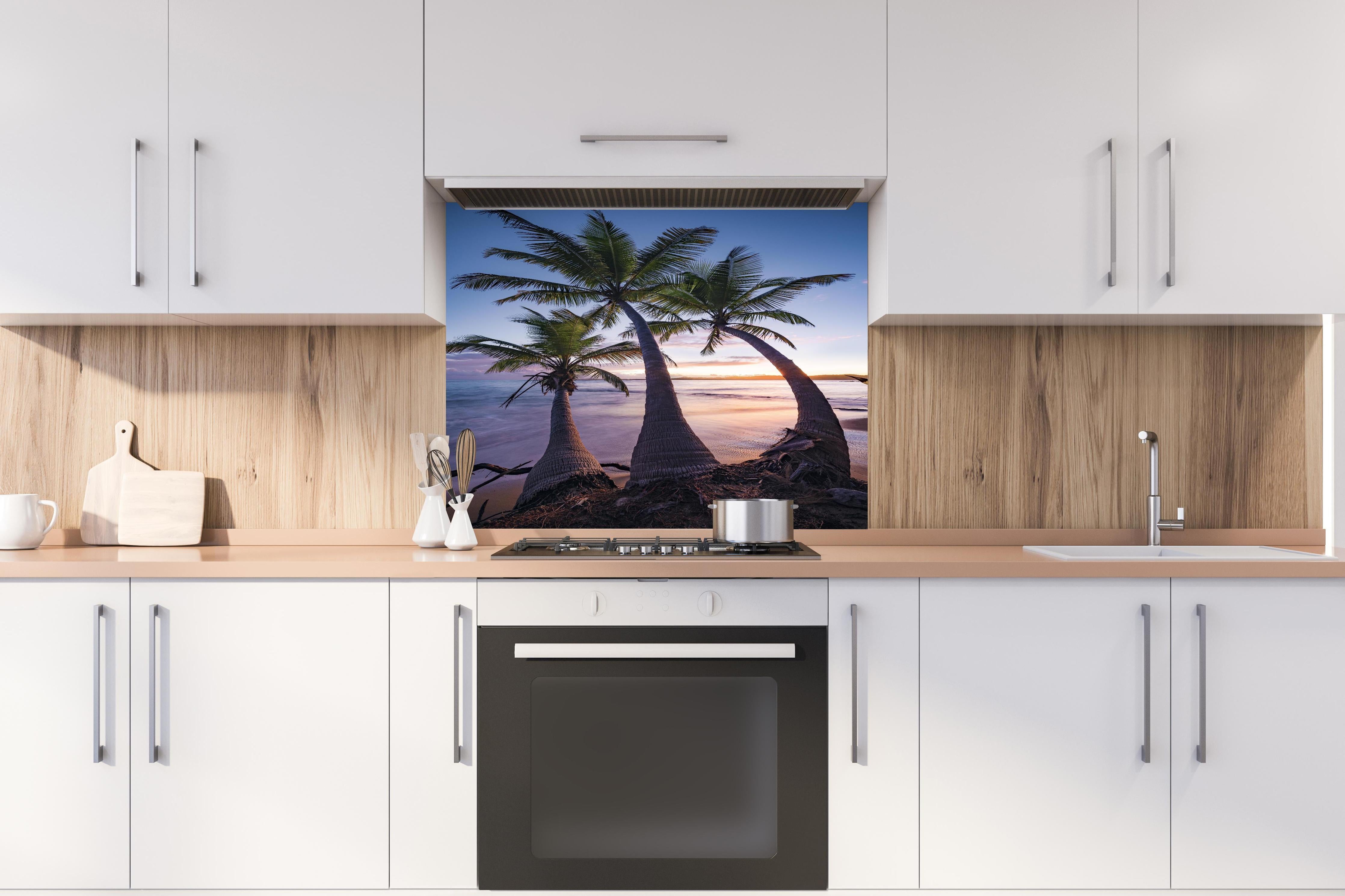 Spritzschutz - Karibik Palmenstrand bei Dämmerung hinter einem Cerankochfeld zwischen Holz-Kochutensilien
