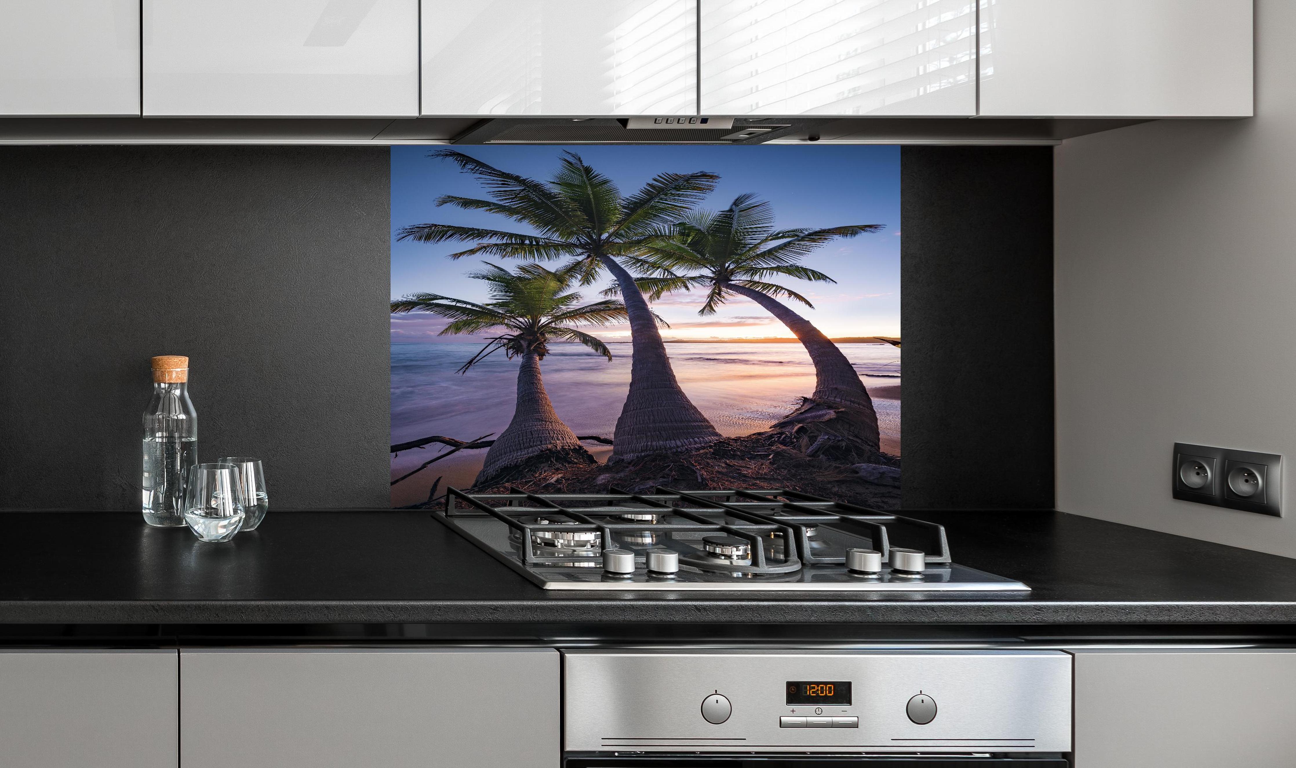 Spritzschutz - Karibik Palmenstrand bei Dämmerung hinter einem Cerankochfeld zwischen Holz-Kochutensilien
