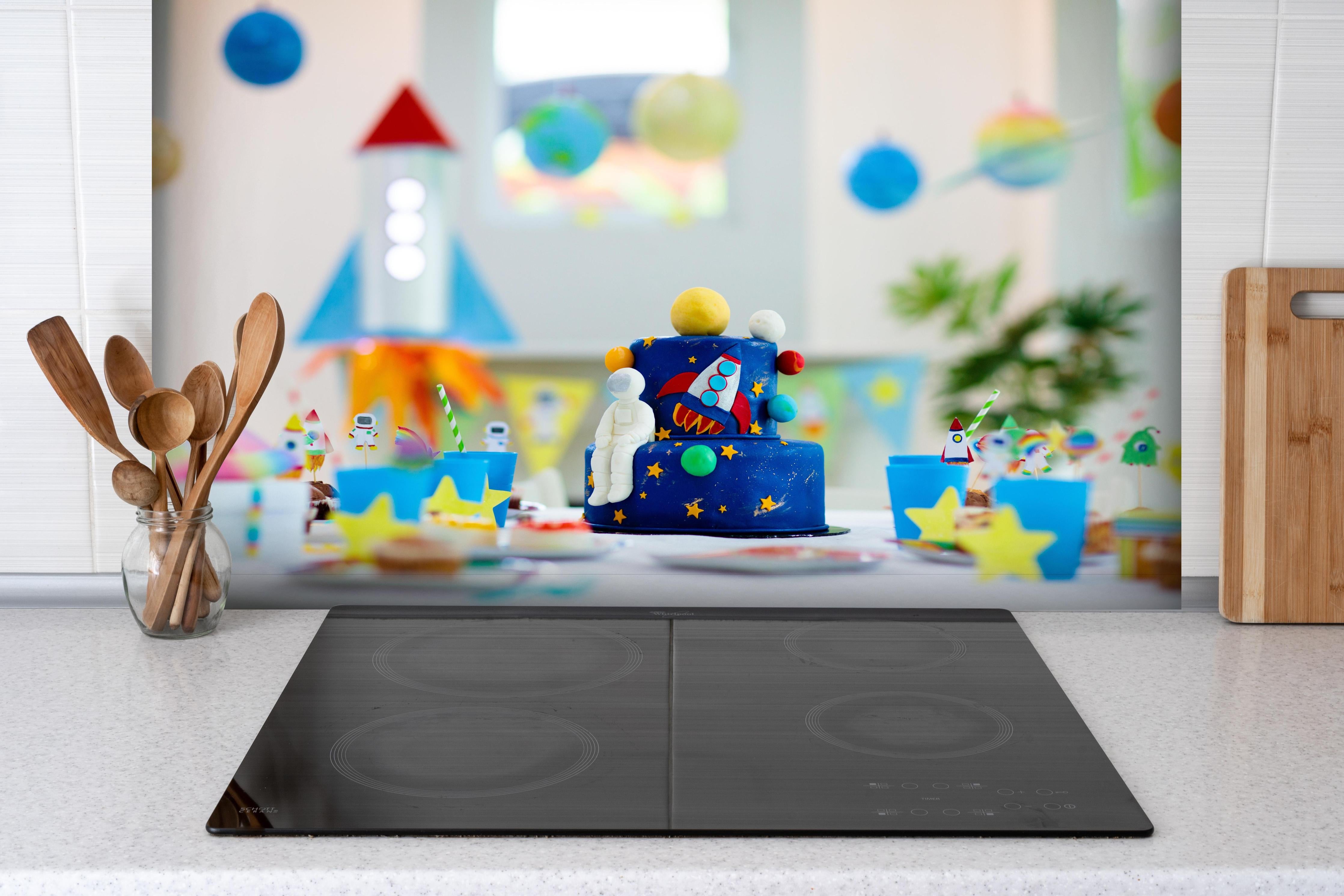 Spritzschutz - Kindergeburtstagsfeier zum Thema Weltraum mit Kuchen. hinter einem Cerankochfeld zwischen Holz-Kochutensilien

