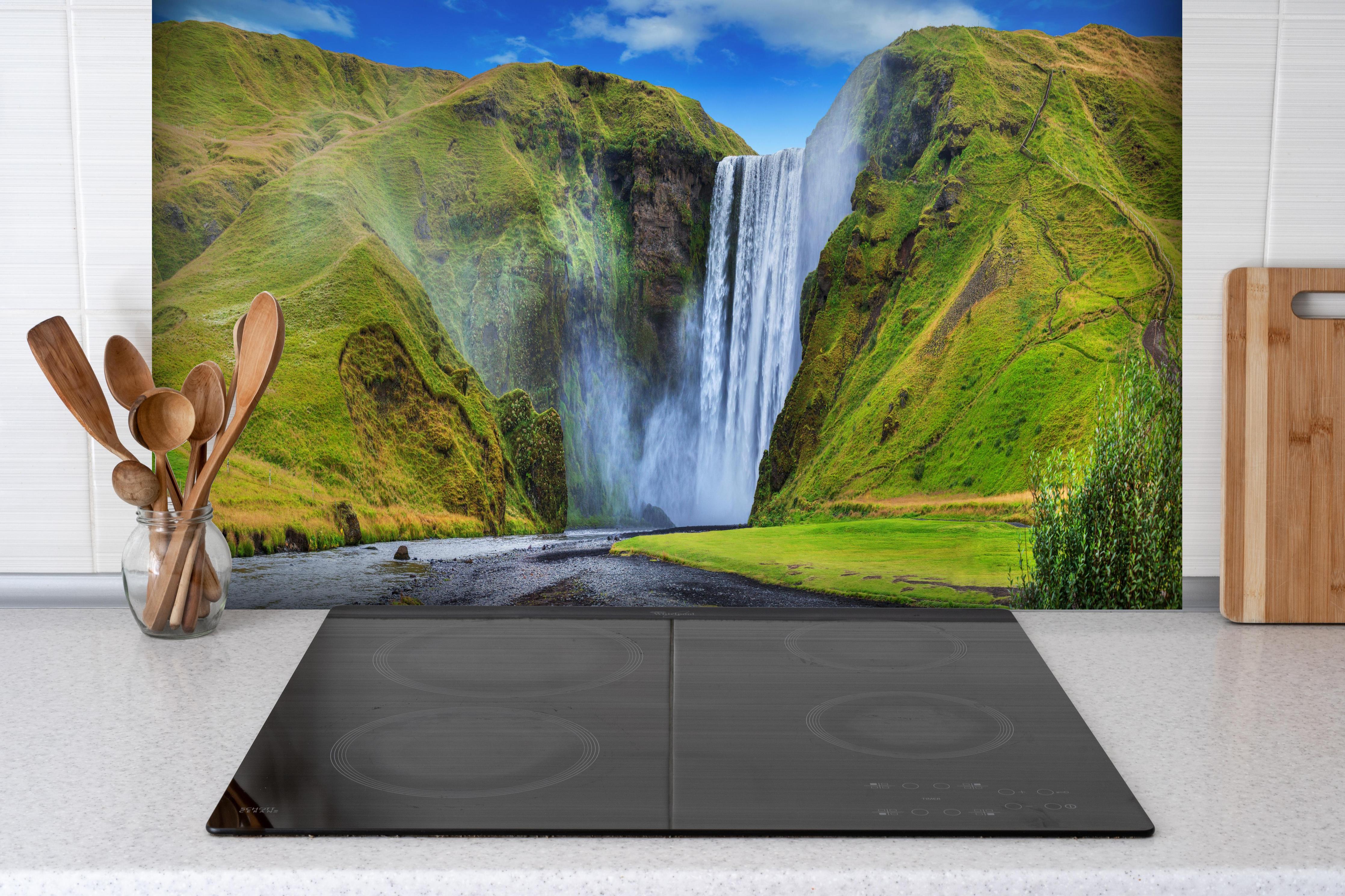 Spritzschutz - Kraftvoller Wasserfall hinter einem Cerankochfeld zwischen Holz-Kochutensilien
