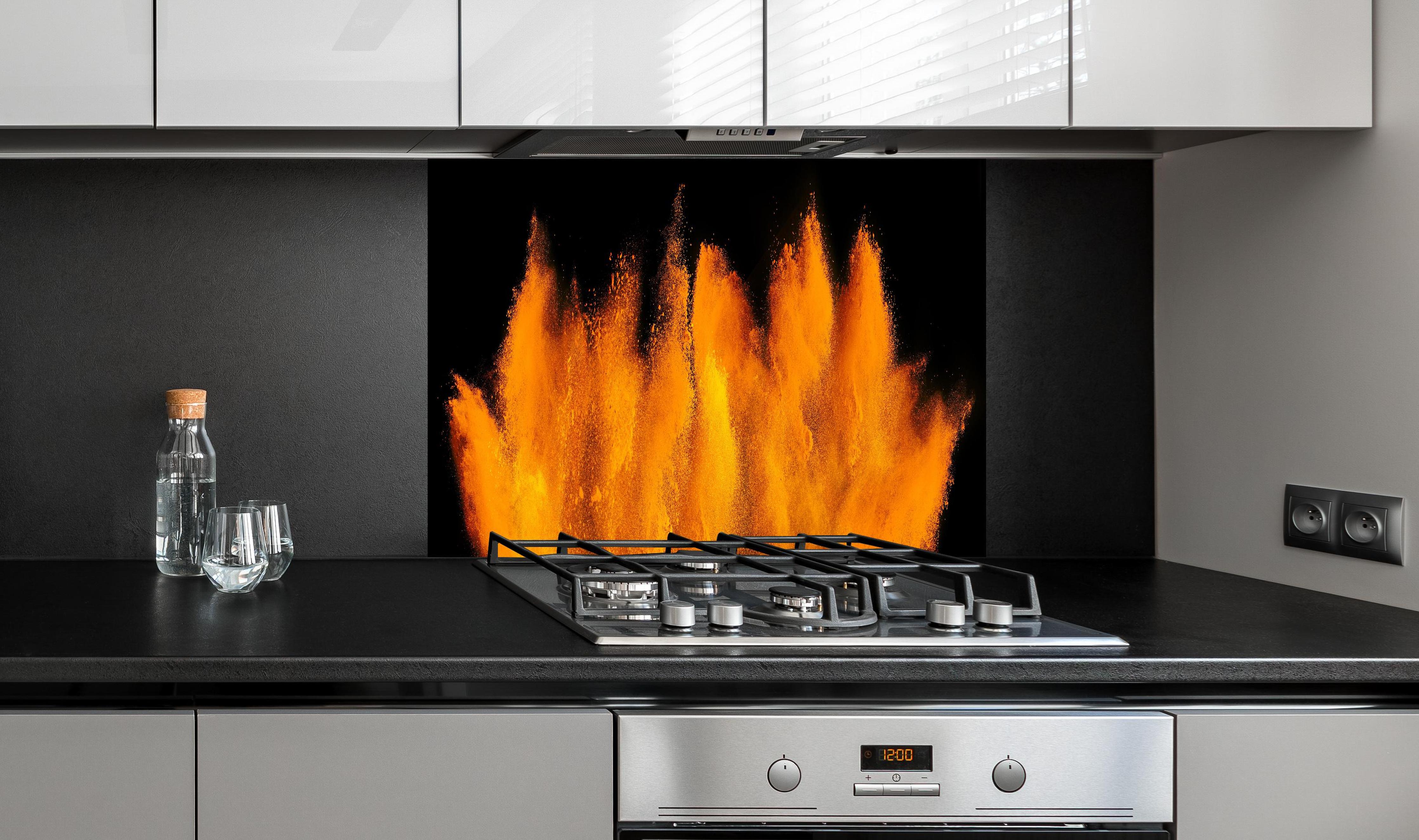 Spritzschutz - Lebendige Holi Farbexplosion auf Schwarz hinter einem Cerankochfeld zwischen Holz-Kochutensilien
