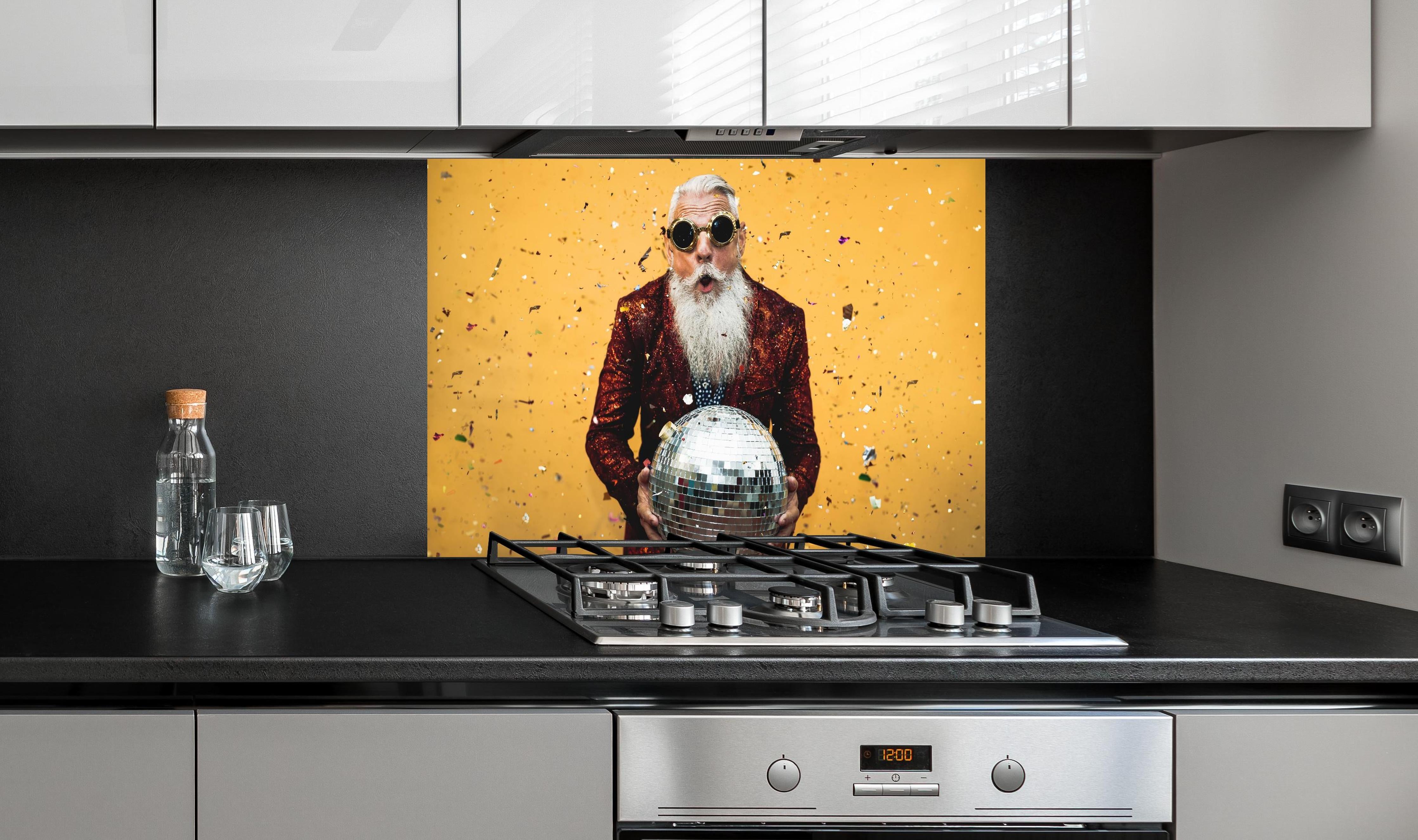Spritzschutz - Lebensfroher Senior feiert mit Discokugel hinter einem Cerankochfeld zwischen Holz-Kochutensilien
