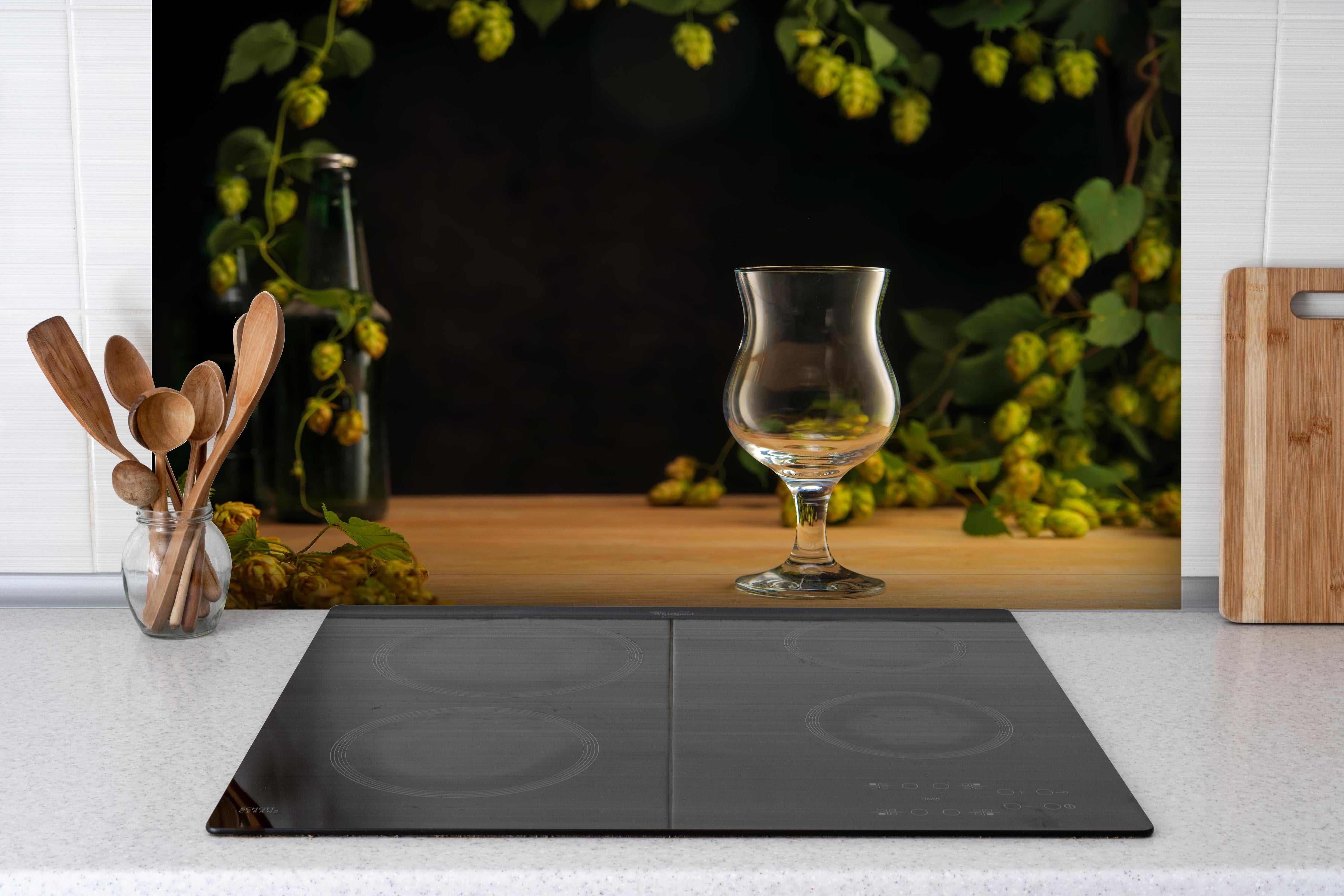 Spritzschutz - Leeres Tulpenglas auf Holztisch hinter einem Cerankochfeld zwischen Holz-Kochutensilien
