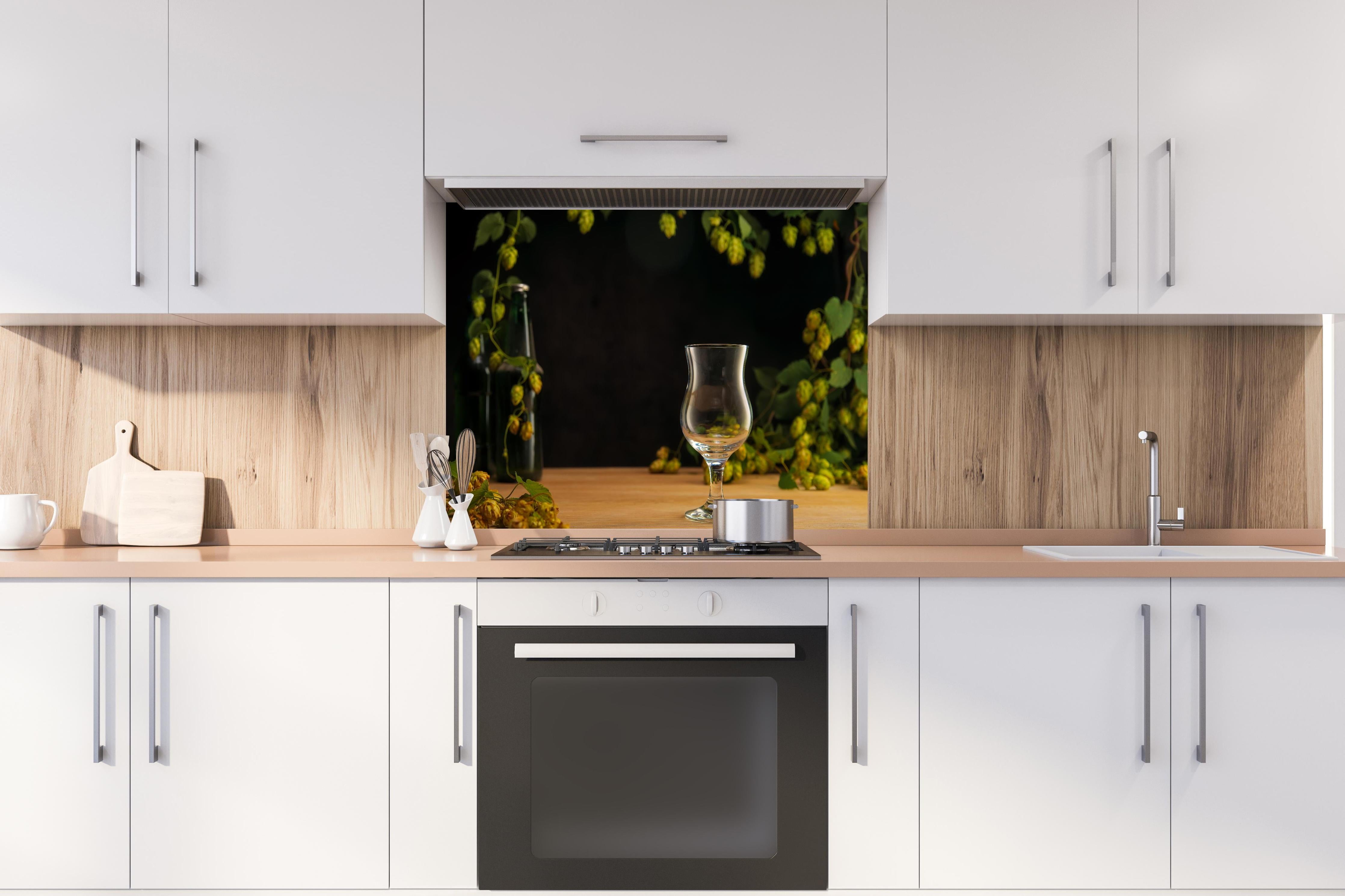 Spritzschutz - Leeres Tulpenglas auf Holztisch hinter einem Cerankochfeld zwischen Holz-Kochutensilien
