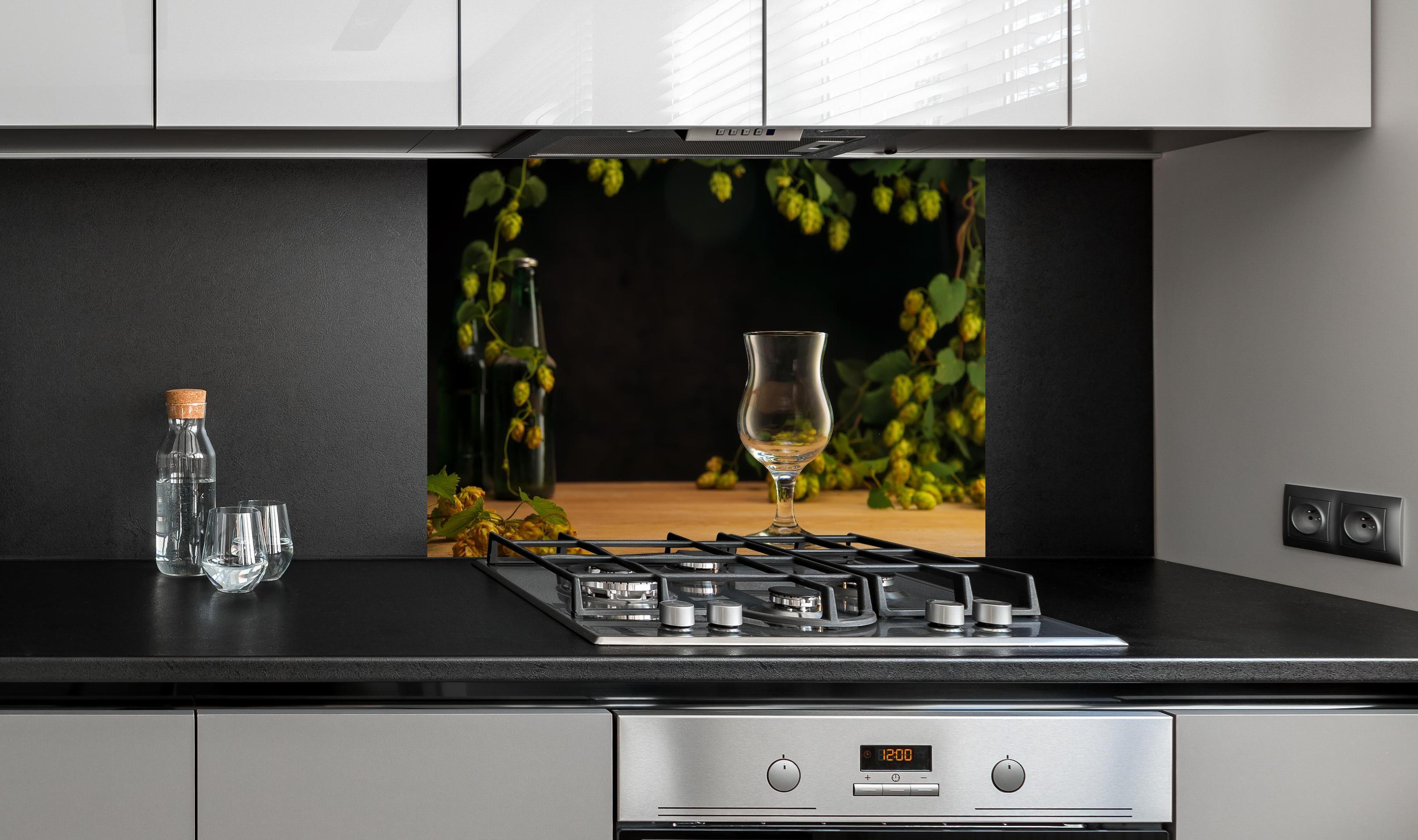 Spritzschutz - Leeres Tulpenglas auf Holztisch hinter einem Cerankochfeld zwischen Holz-Kochutensilien
