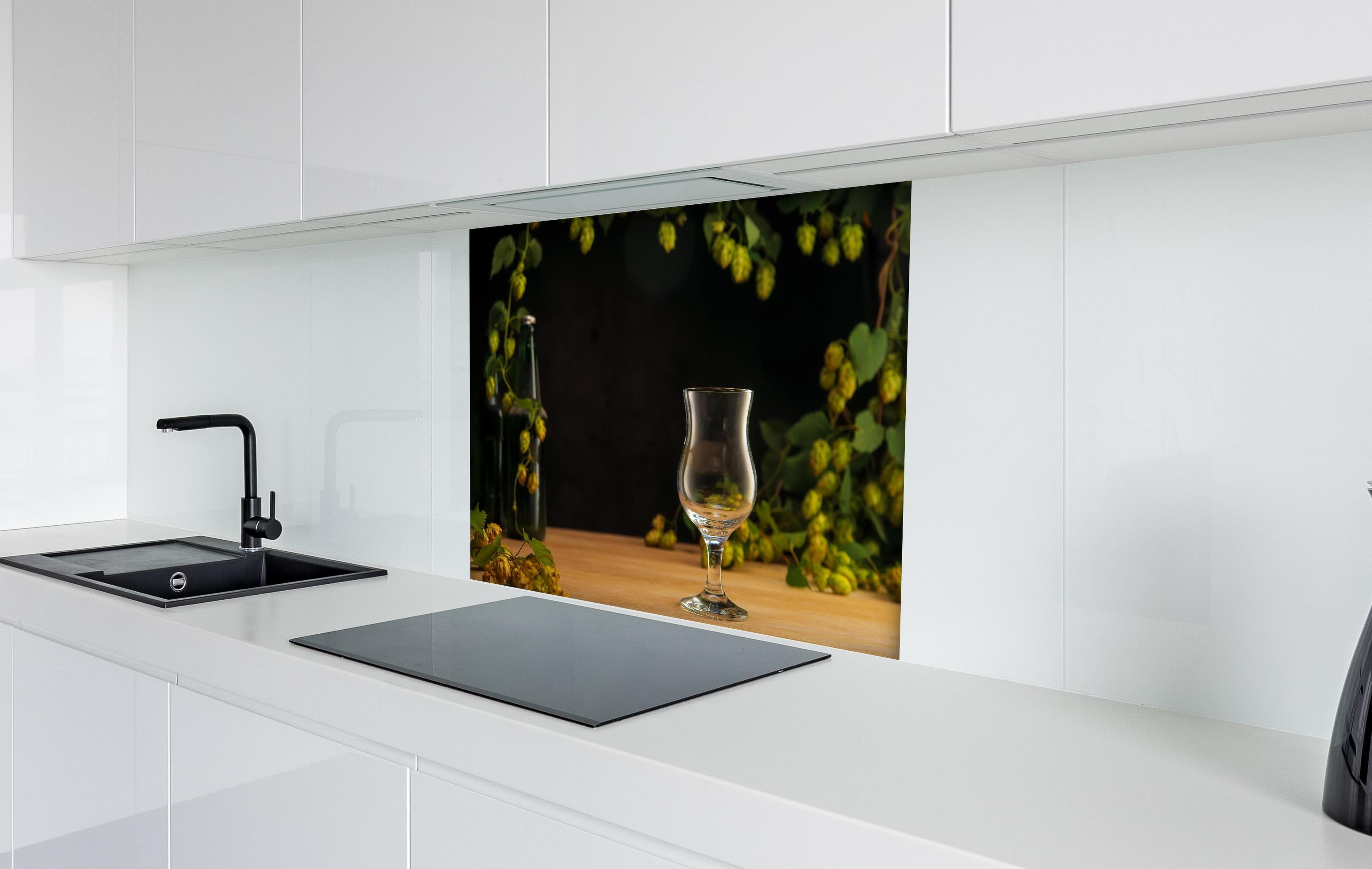 Spritzschutz - Leeres Tulpenglas auf Holztisch hinter einem Cerankochfeld zwischen Holz-Kochutensilien
