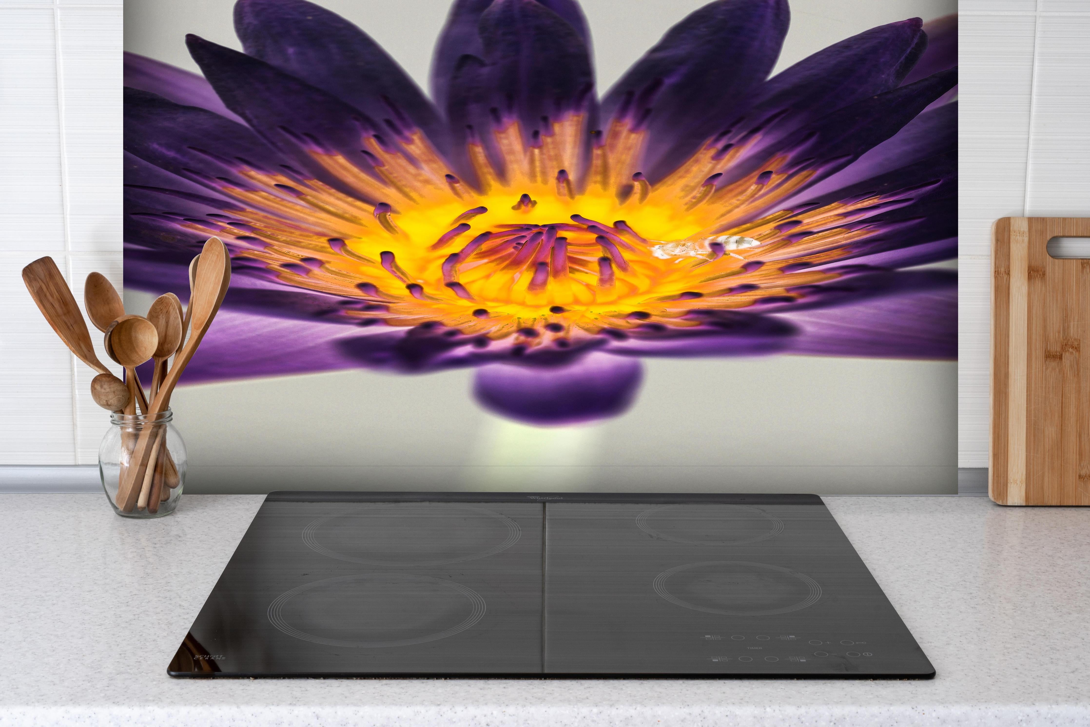 Spritzschutz - Leuchtende Lila Wasserlilie mit gelbem Kern Makro hinter einem Cerankochfeld zwischen Holz-Kochutensilien
