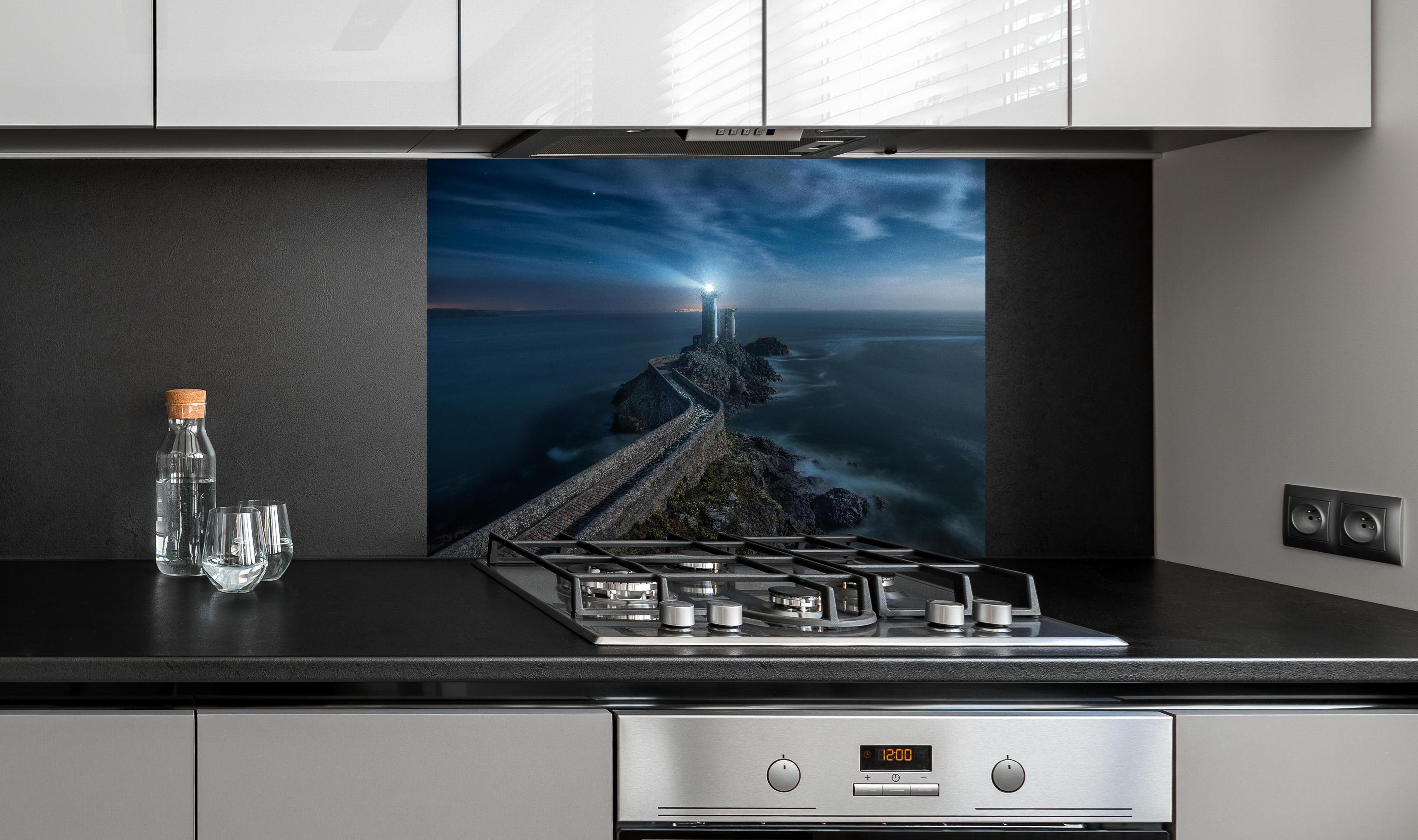 Spritzschutz - Leuchtturm - Nächtlich hinter einem Cerankochfeld zwischen Holz-Kochutensilien
