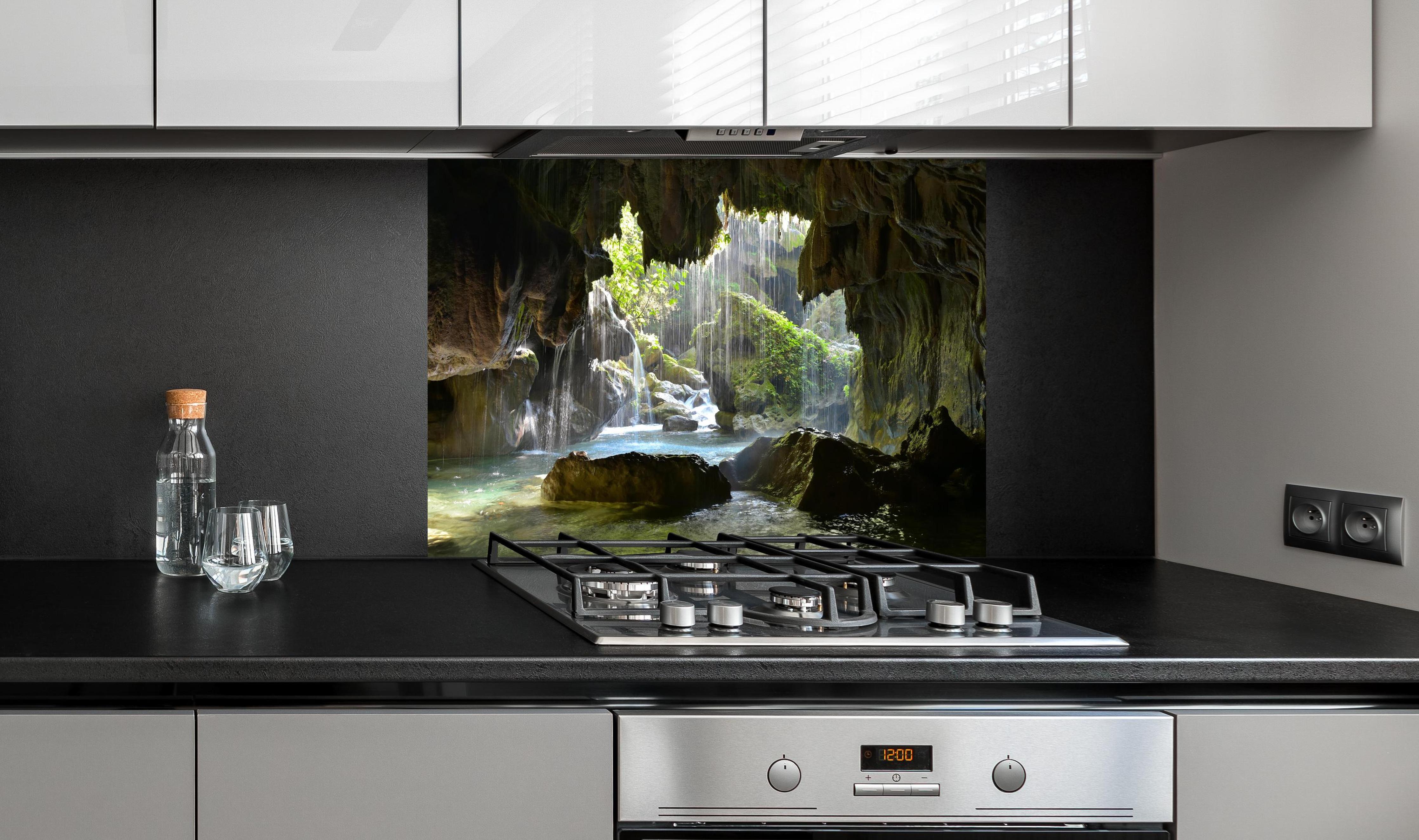 Spritzschutz - Lichtdurchflutete Grüne Höhlenlandschaft hinter einem Cerankochfeld zwischen Holz-Kochutensilien
