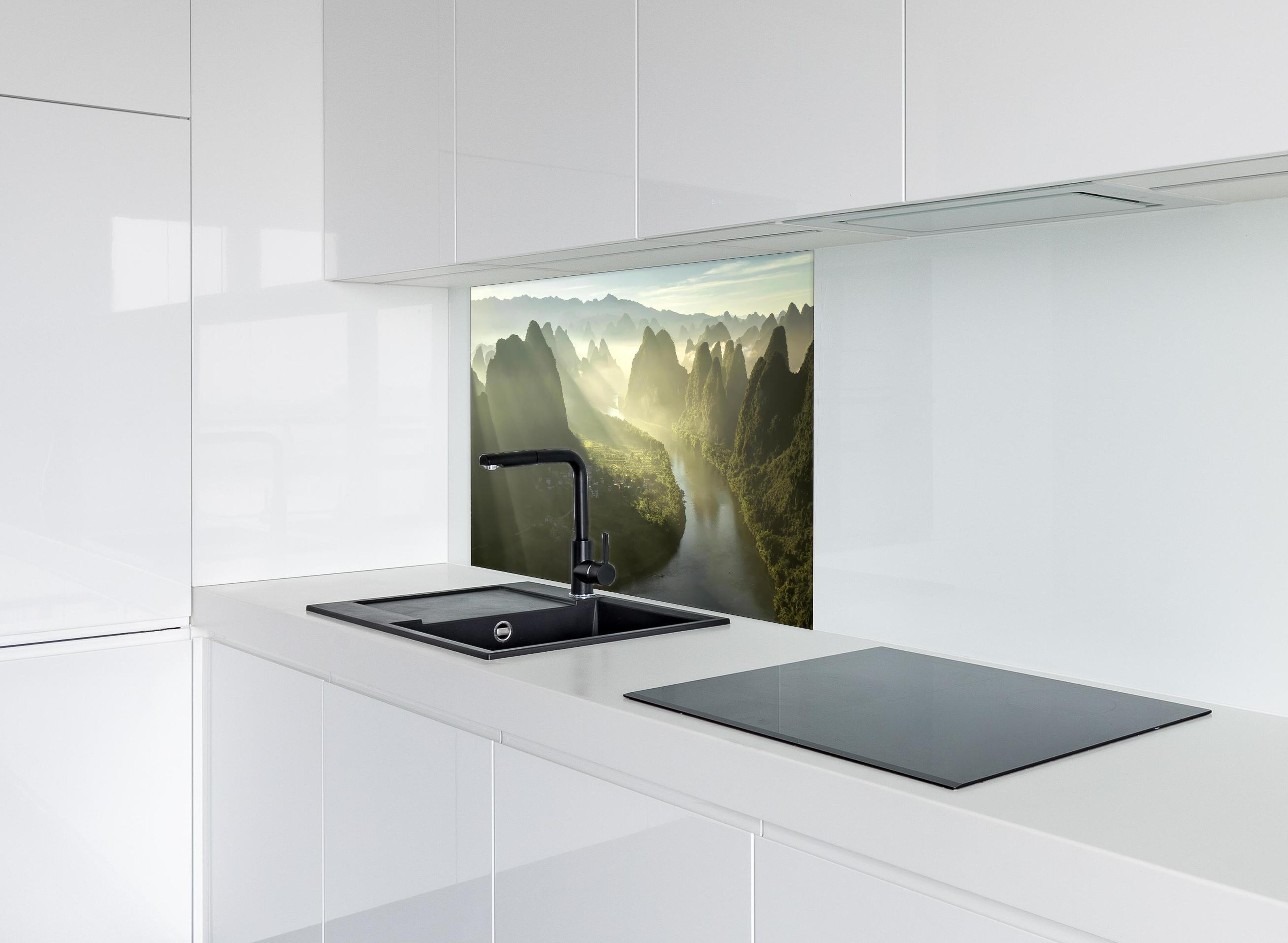 Spritzschutz - Lichtstrahlen über Li-Fluss und Karstberge hinter einem Cerankochfeld zwischen Holz-Kochutensilien
