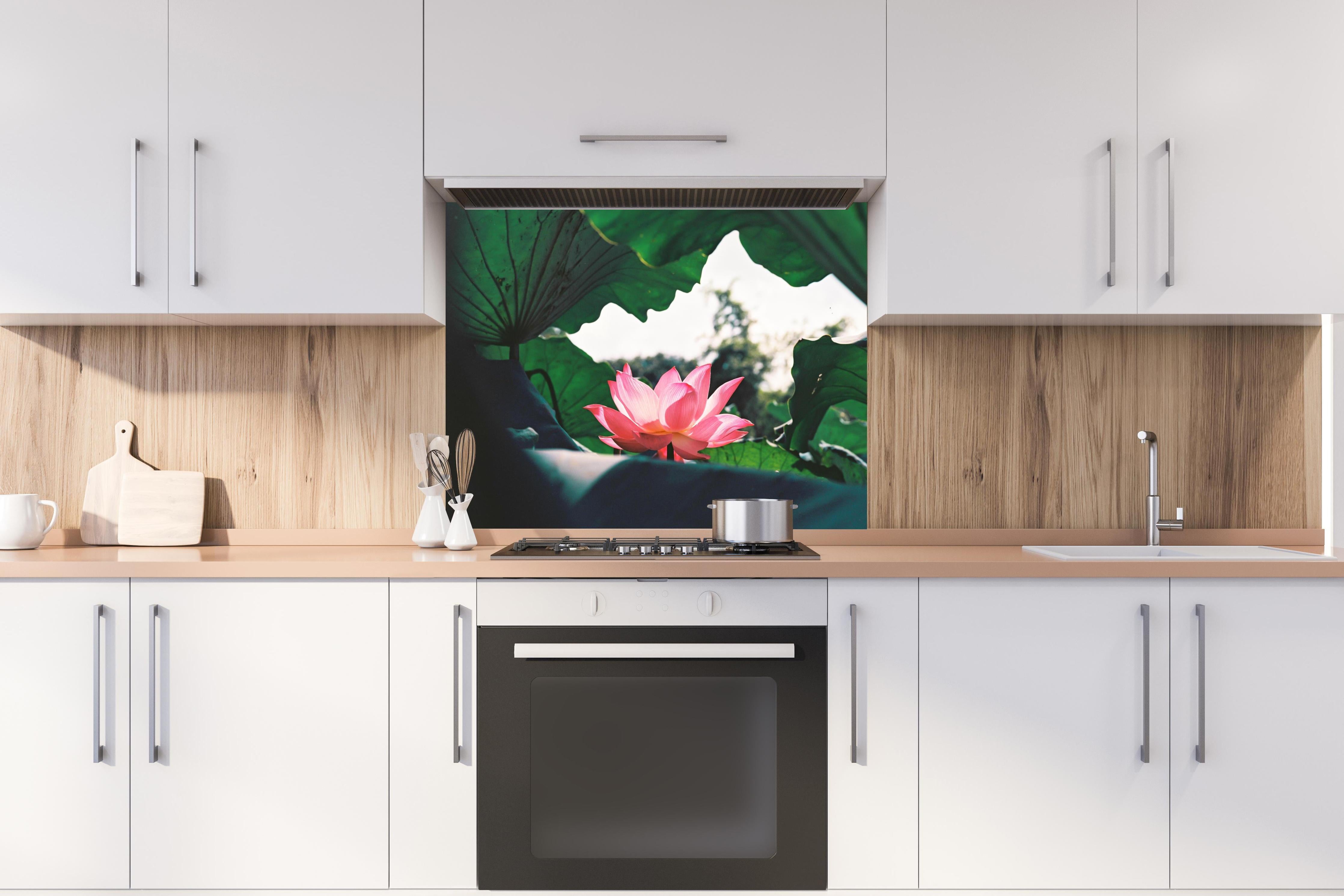 Spritzschutz - Lotosblume inmitten von Blättern hinter einem Cerankochfeld zwischen Holz-Kochutensilien
